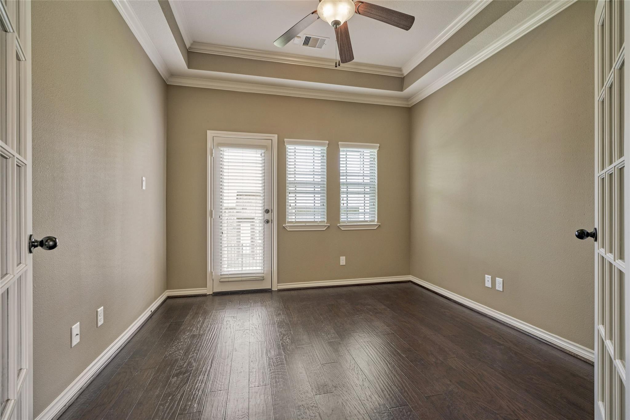 Empty room with dark flooring, tray ceiling, ceiling fan, and a glass door with blinds.