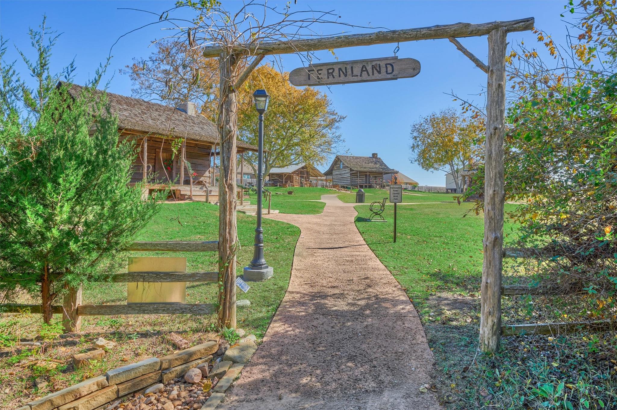 Landscaped grounds with rustic timber buildings and a path beneath a wooden Fernland sign.