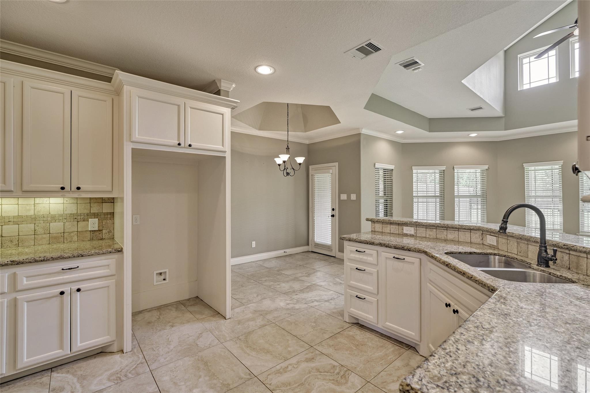 Kitchen with white cabinets, granite counters, double sink, and a high ceiling opening to a dining area.