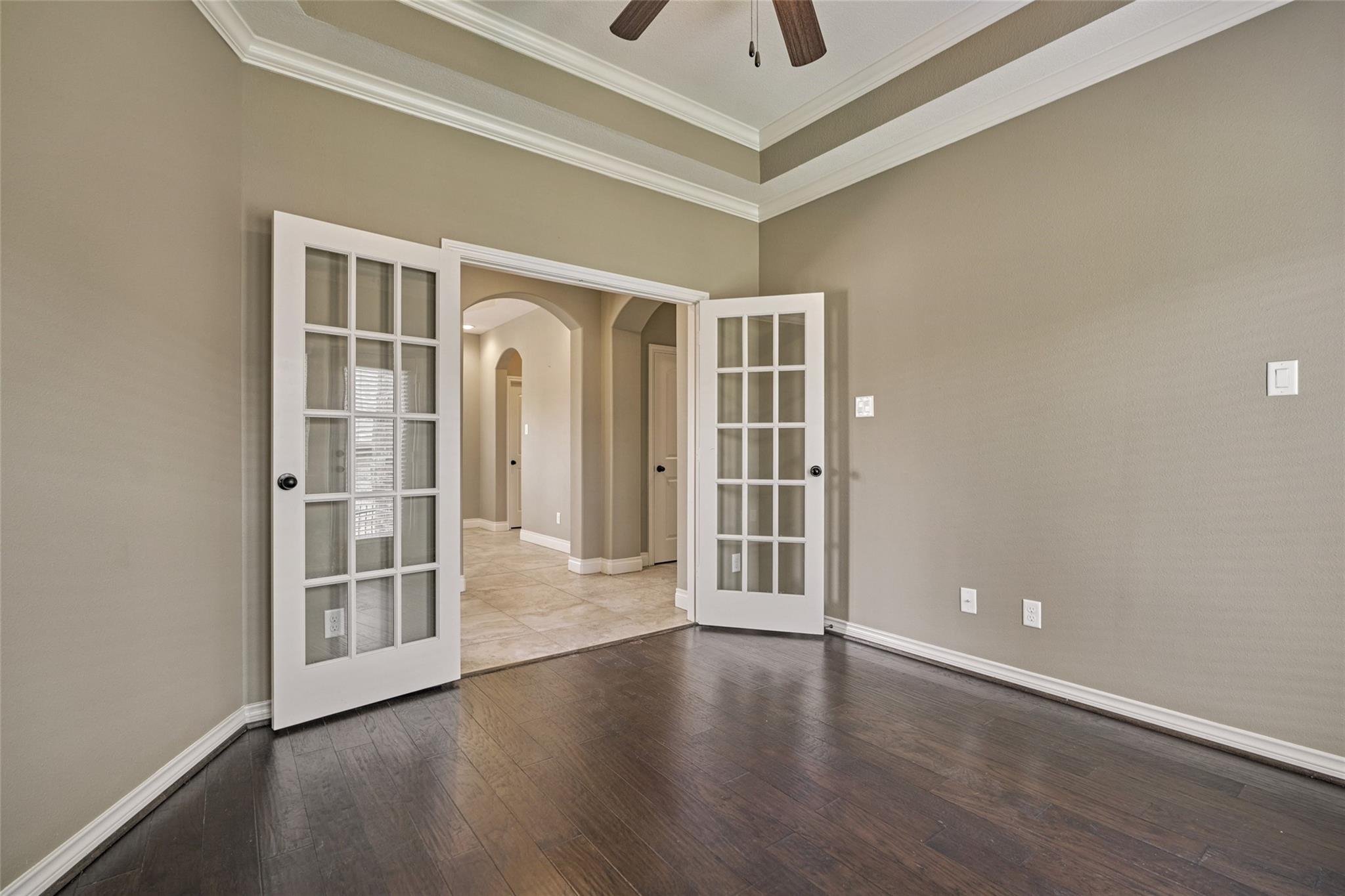 Empty room with dark wood floors and open French doors leading to an arched tiled hallway.