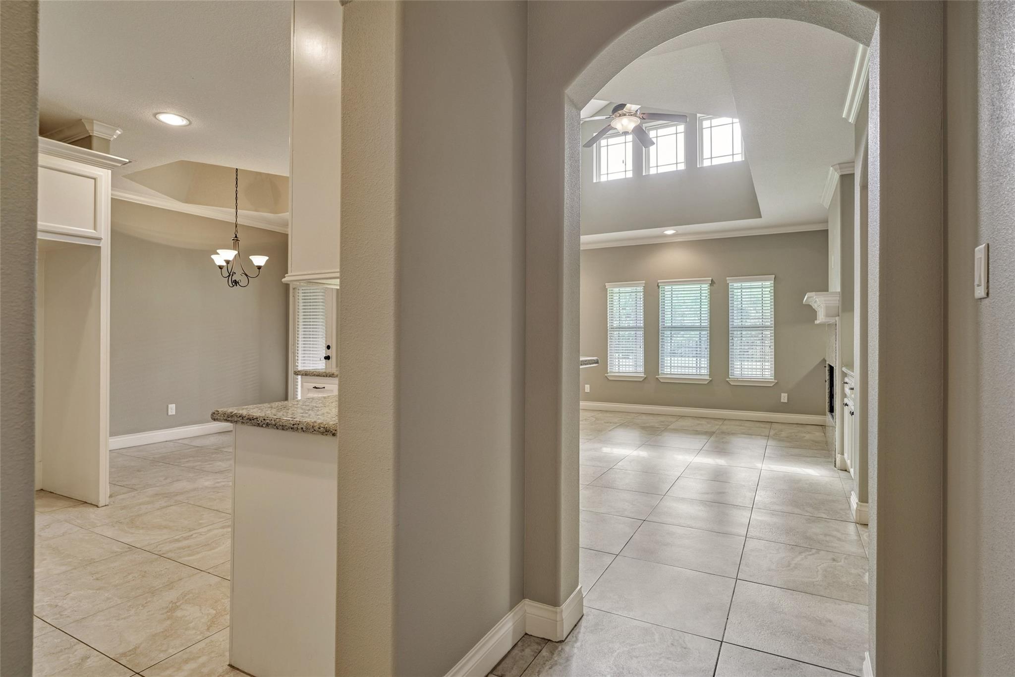 Open-plan interior with tiled floors, granite counter, arched opening, and vaulted living area with tall windows.