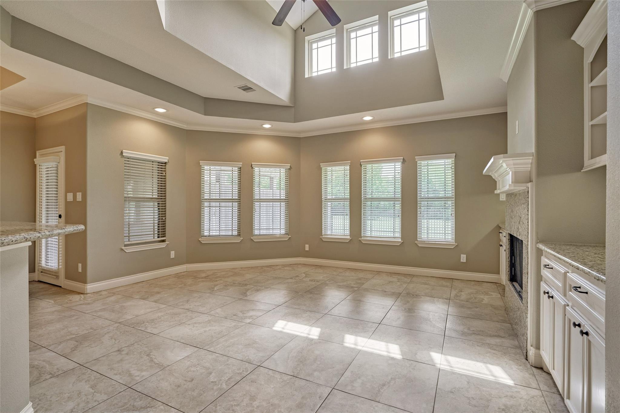 Empty living room with a vaulted ceiling, tiled floors, many windows, and a fireplace.