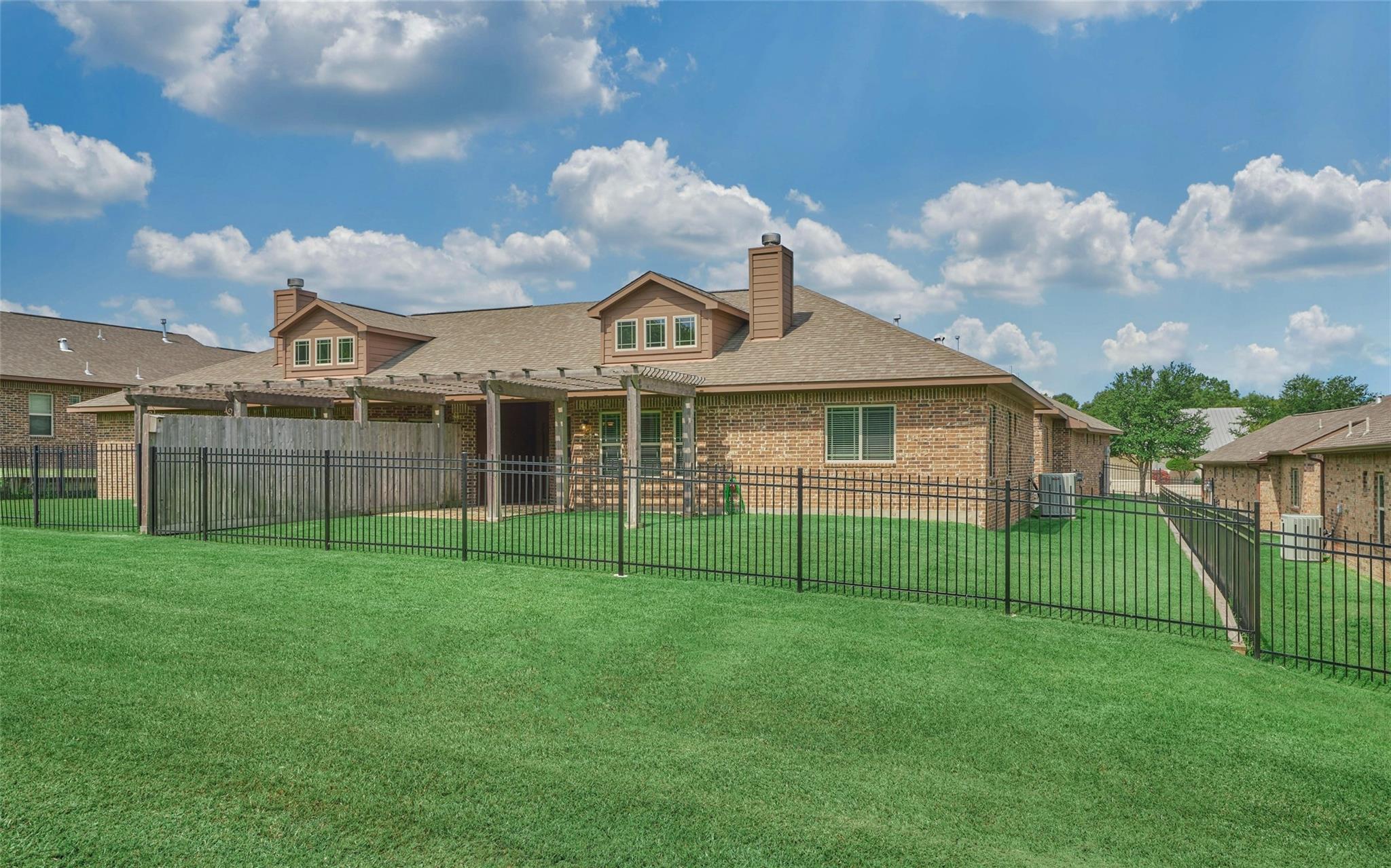 Brick home’s rear exterior with a pergola-covered patio and fenced lawn.