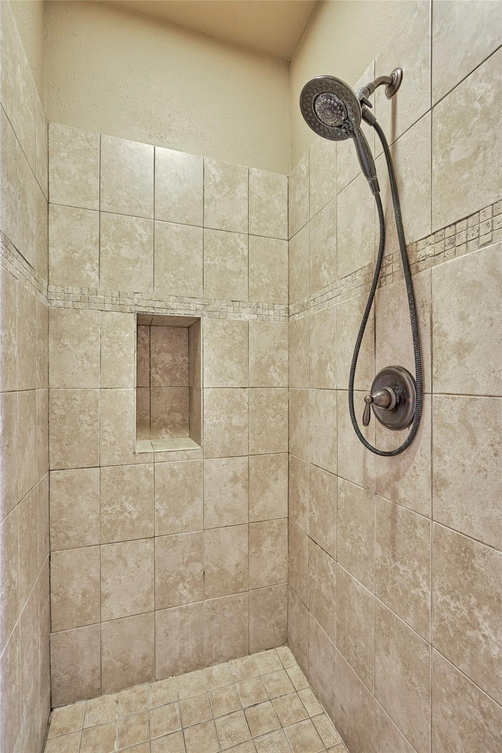 Tiled walk-in shower with a recessed niche and dark bronze handheld showerhead.