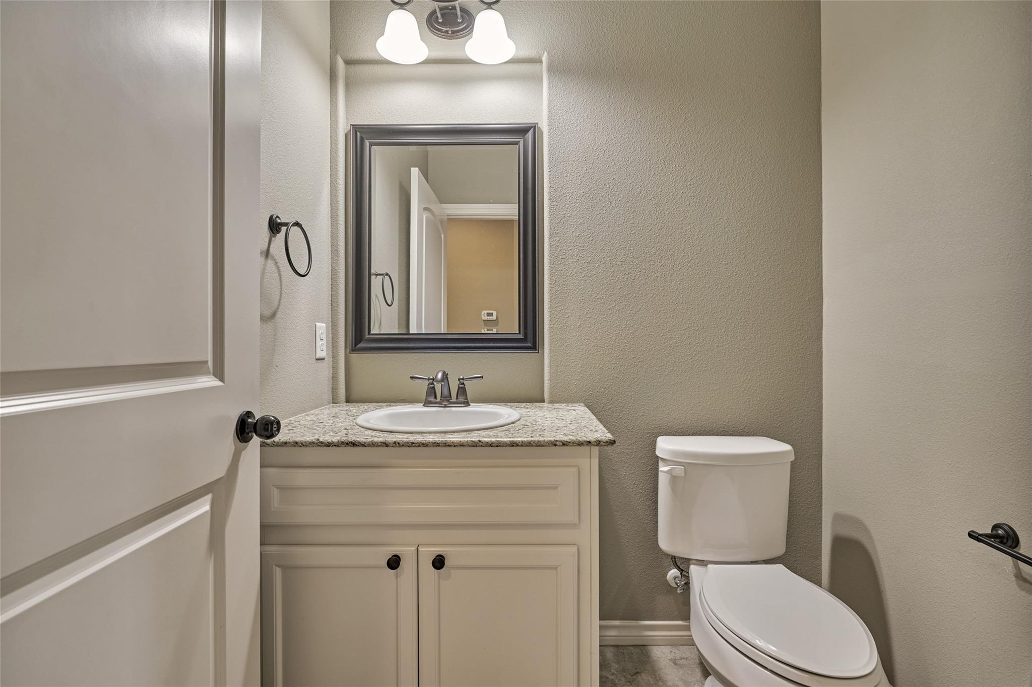 Bathroom with a white vanity, stone countertop, framed mirror, and toilet.