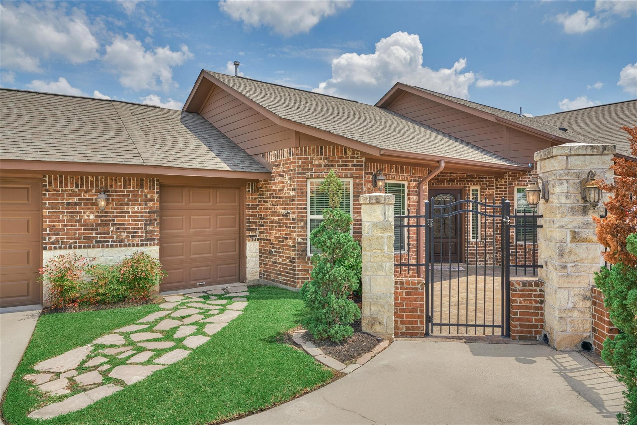 Brick home with brown garage doors and a gated entry framed by stone pillars.