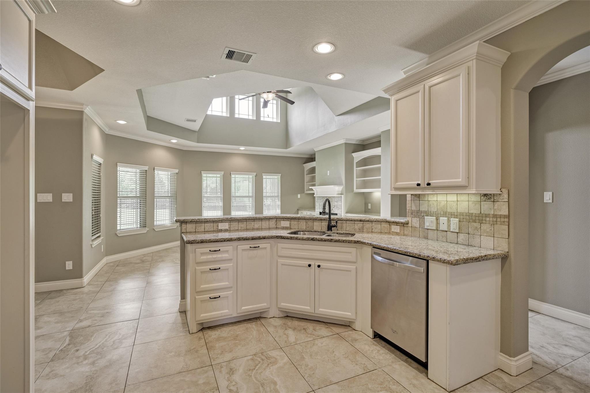 Kitchen with cream cabinetry, granite counters, stainless dishwasher, and a raised ceiling with clerestory windows.