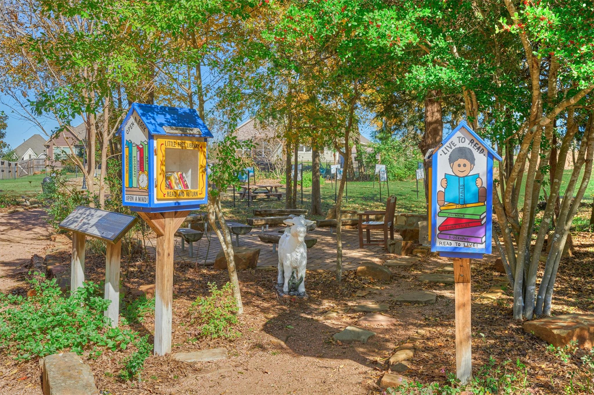Shaded reading garden with colorful little free library boxes, benches, and a stone path.