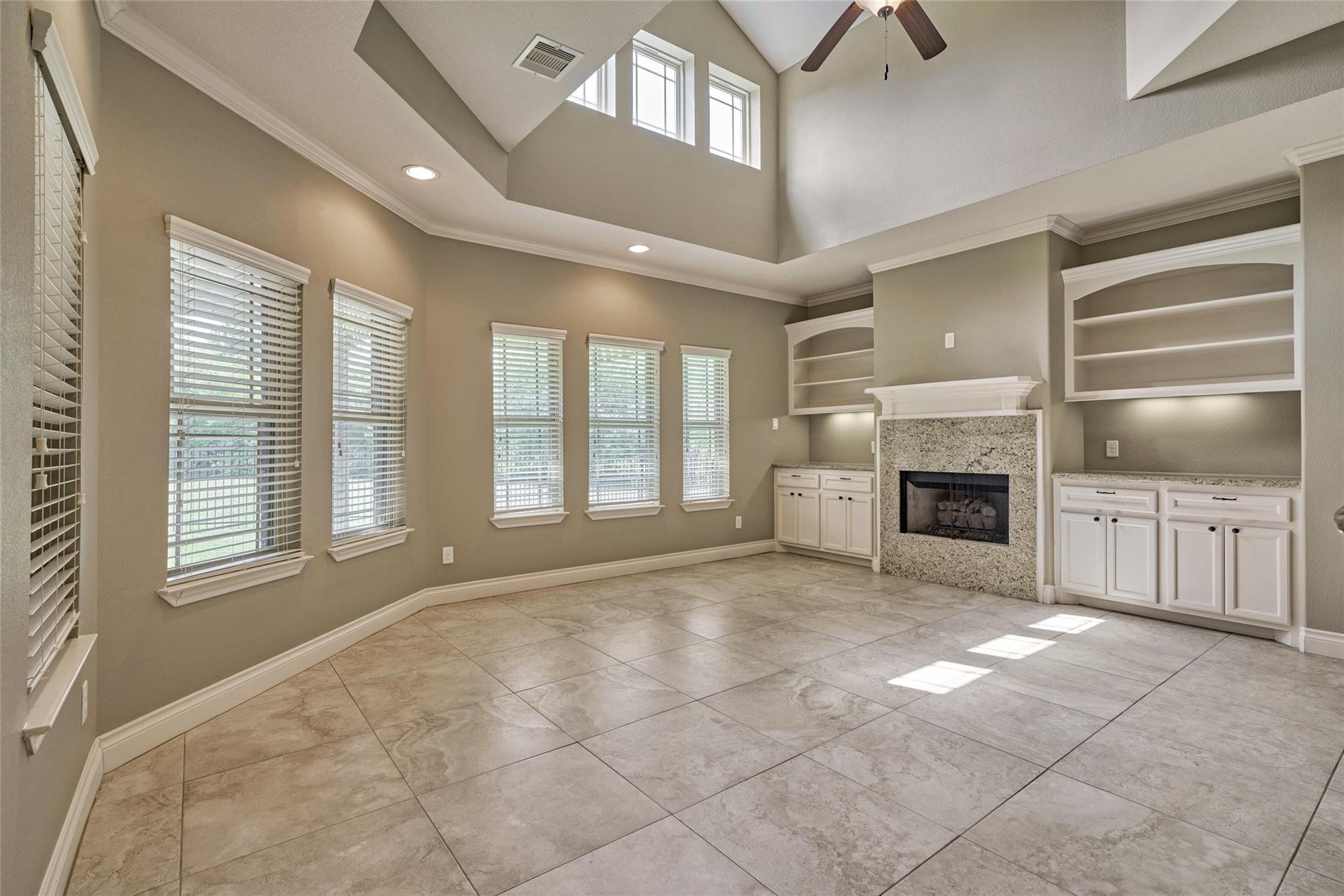 Vacant living room with vaulted ceiling, tiled floors, and a fireplace framed by built-in shelves.