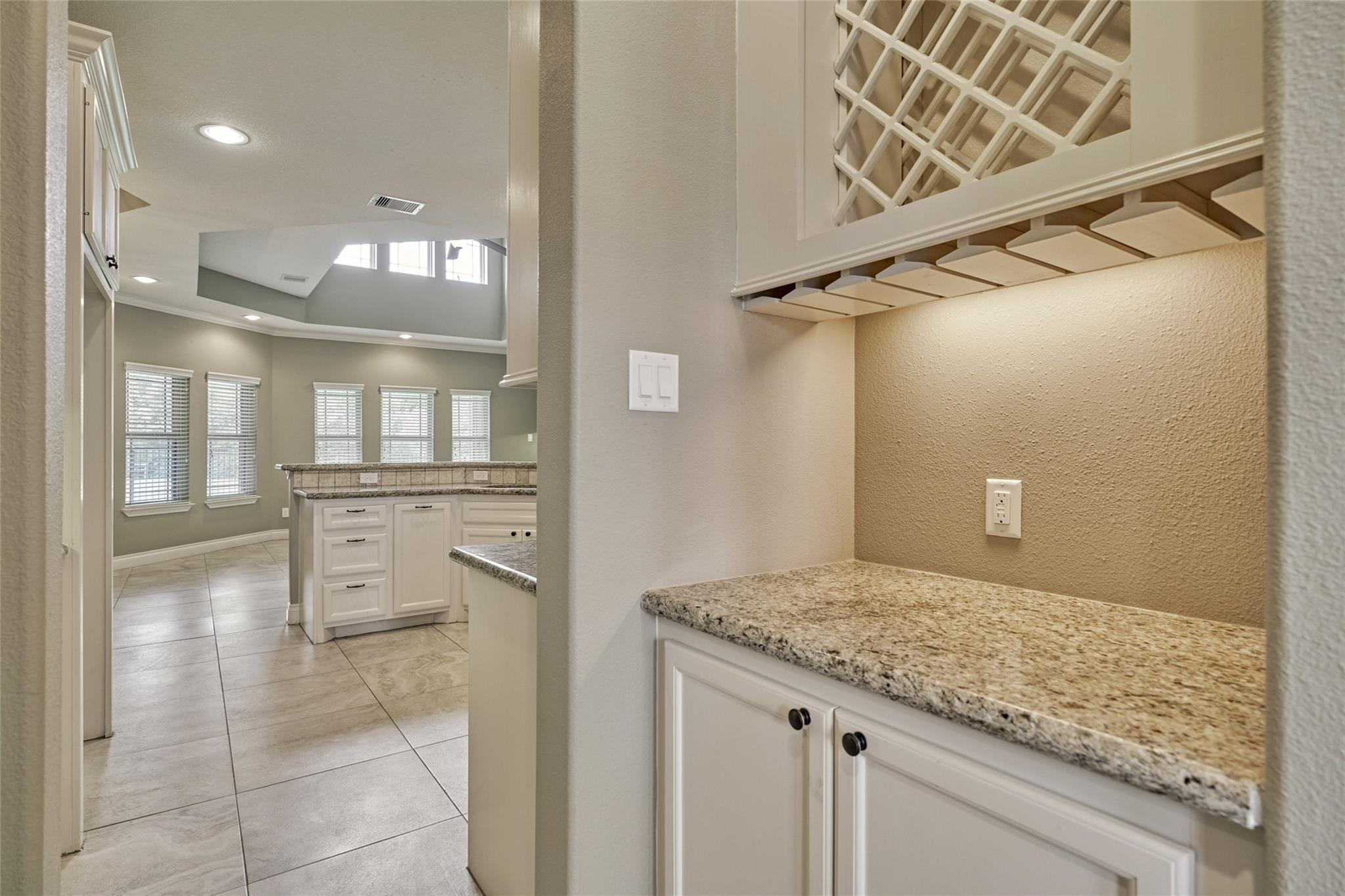 Kitchen with white cabinets, granite countertops, a built-in wine rack, and large tiled floors.