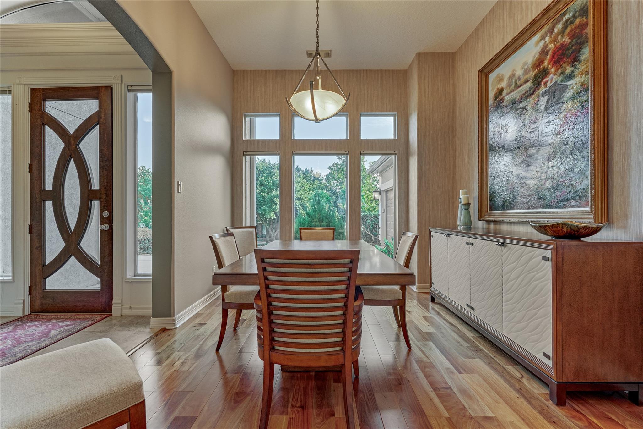 Dining room with a wooden table and chairs, large windows, and a white sculpted-front sideboard.