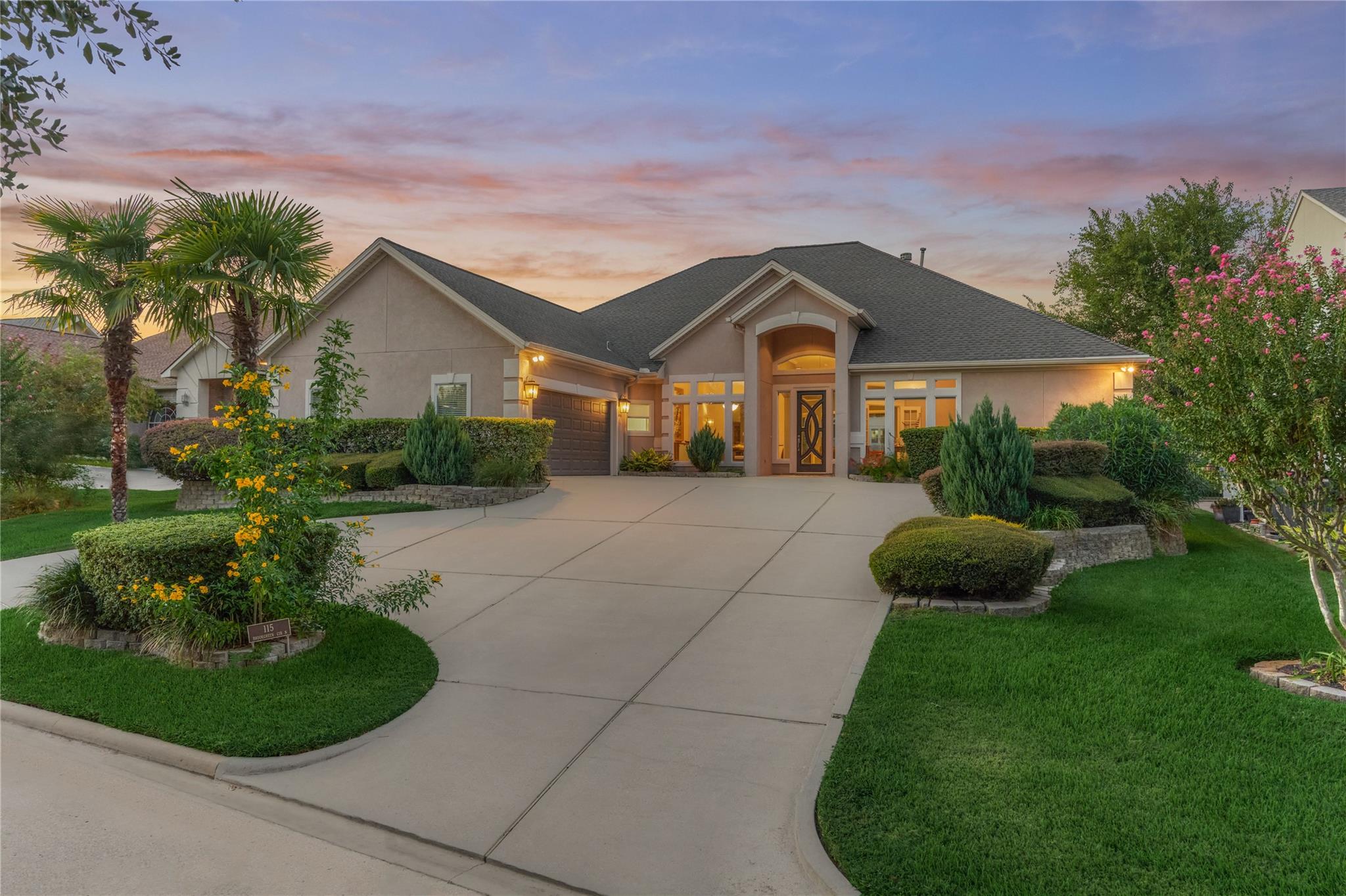 Single-story home with a wide driveway, landscaped lawn, and palm trees at dusk.