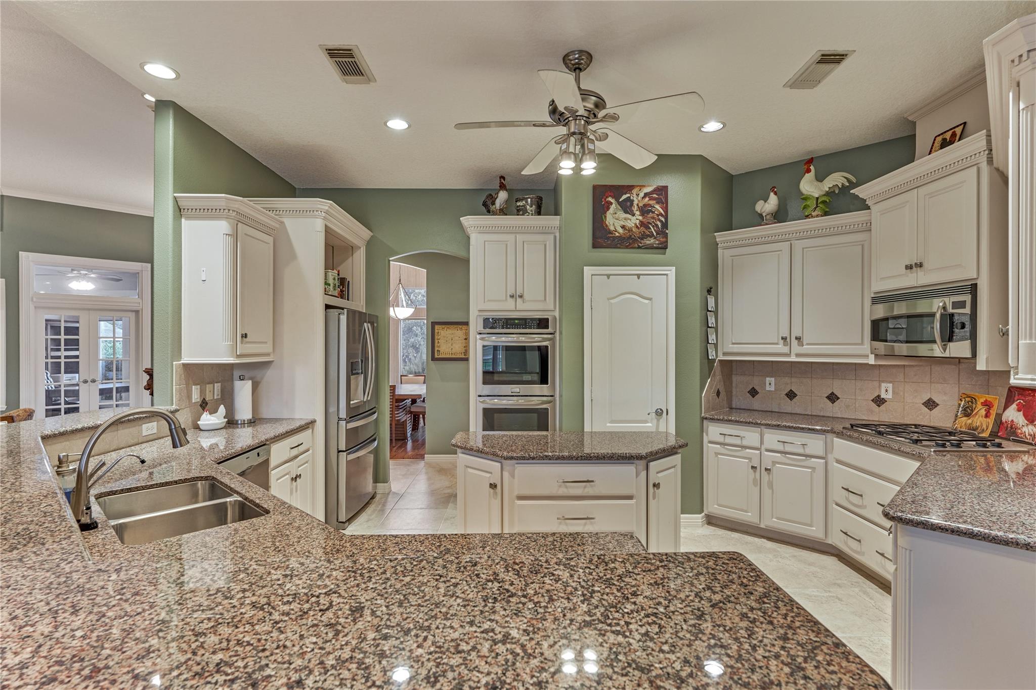 Kitchen with granite counters, a large island, white cabinetry, and stainless steel appliances.