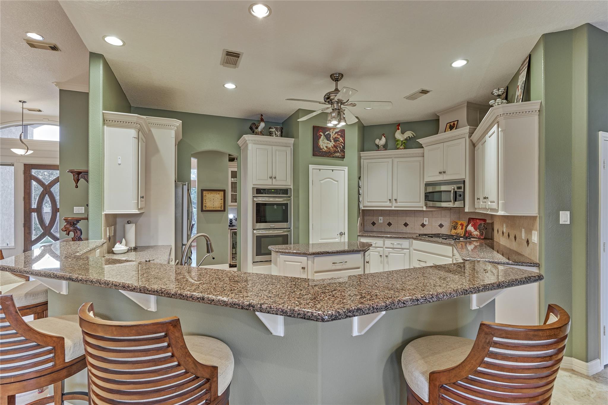 Kitchen with white cabinets, double ovens, granite counters, and a curved breakfast bar with wooden stools.