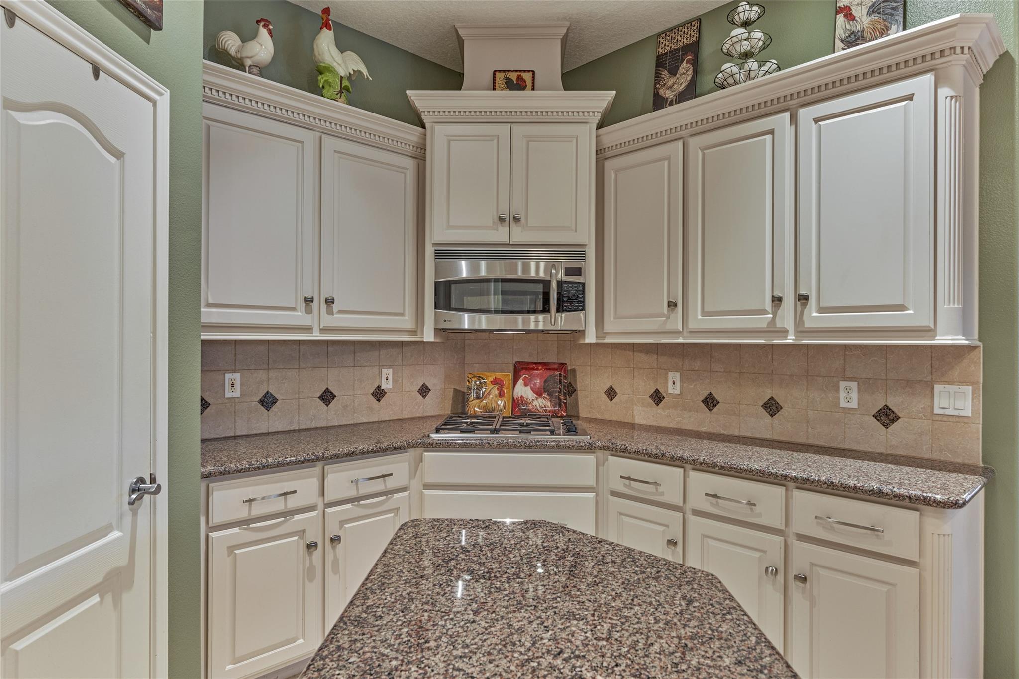 Kitchen with white paneled cabinets, granite counters, a gas cooktop, and rooster decorations.