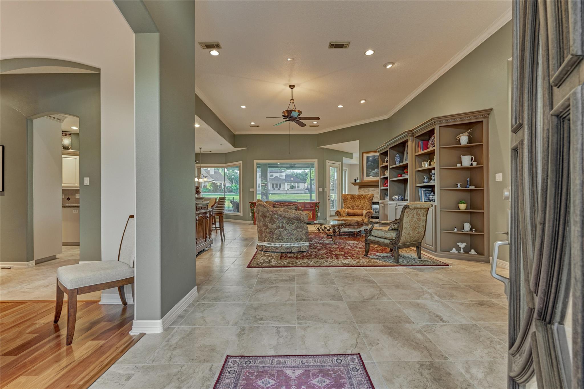Living room with built-in shelves, a tray ceiling, tiled floors, and large windows overlooking the yard.