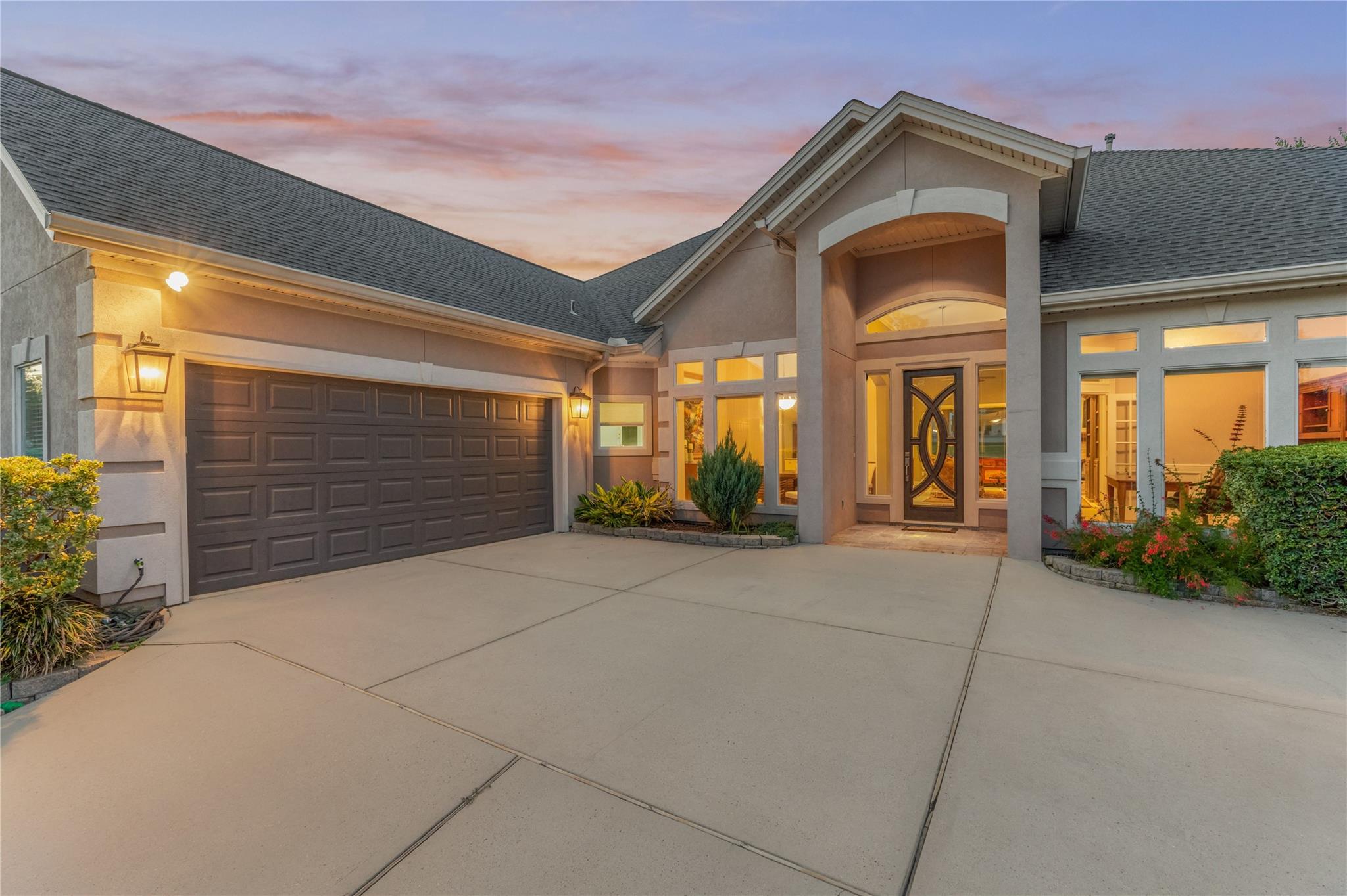 Home exterior at dusk with a wide driveway, double garage, and illuminated arched entry.