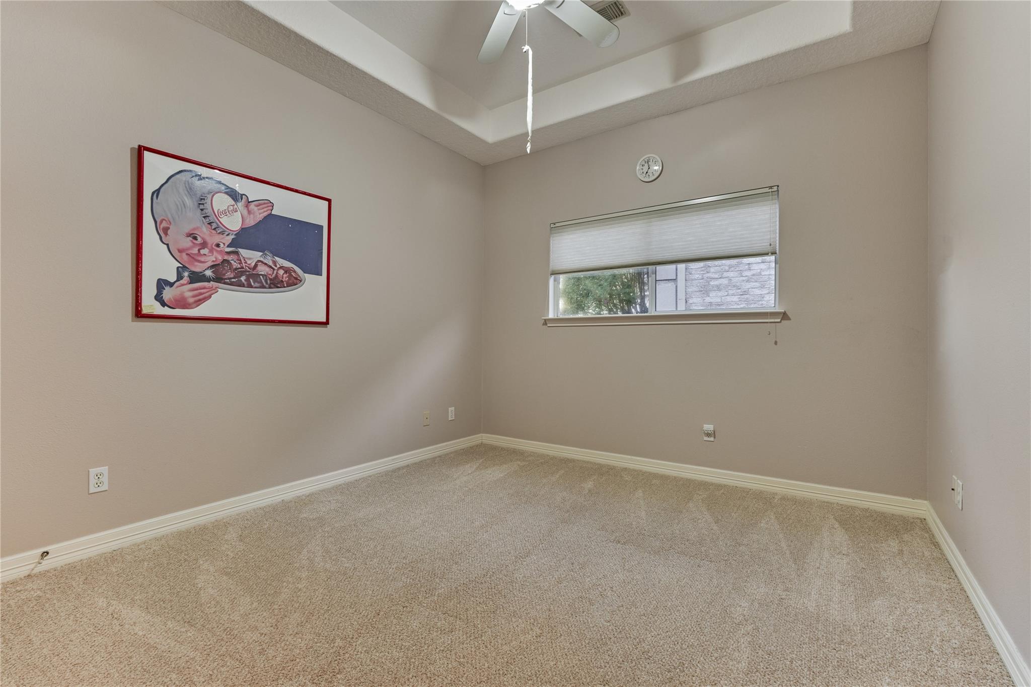 Empty carpeted room with a ceiling fan, small window, and framed Coca-Cola advertisement.