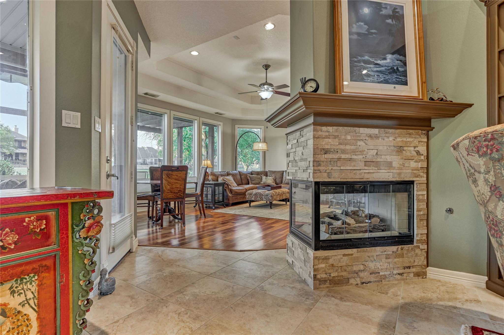 Living room with a stone fireplace, leather seating, hardwood floors, and windows overlooking the yard.