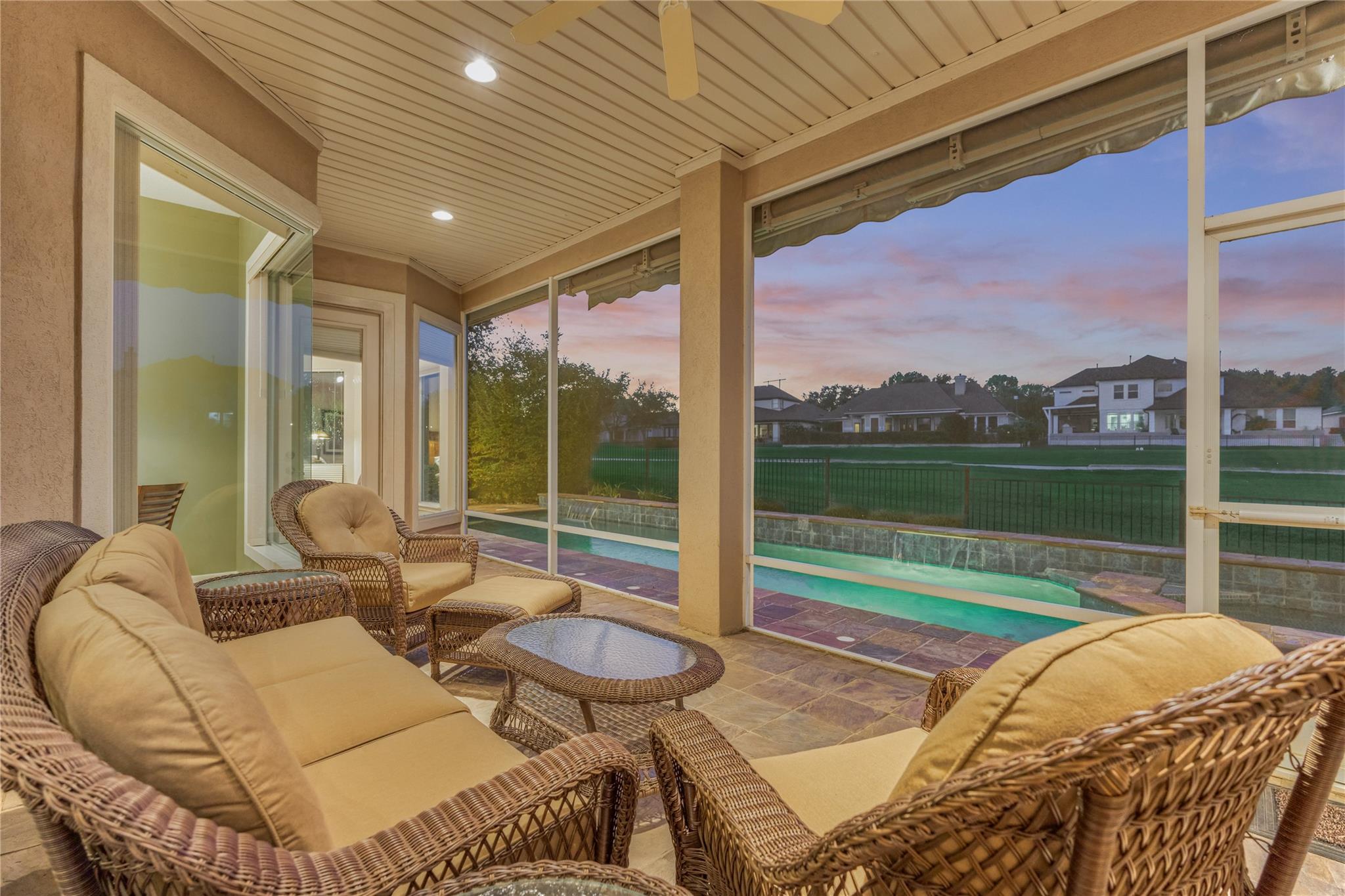 Covered patio with wicker seating overlooking a swimming pool at dusk.