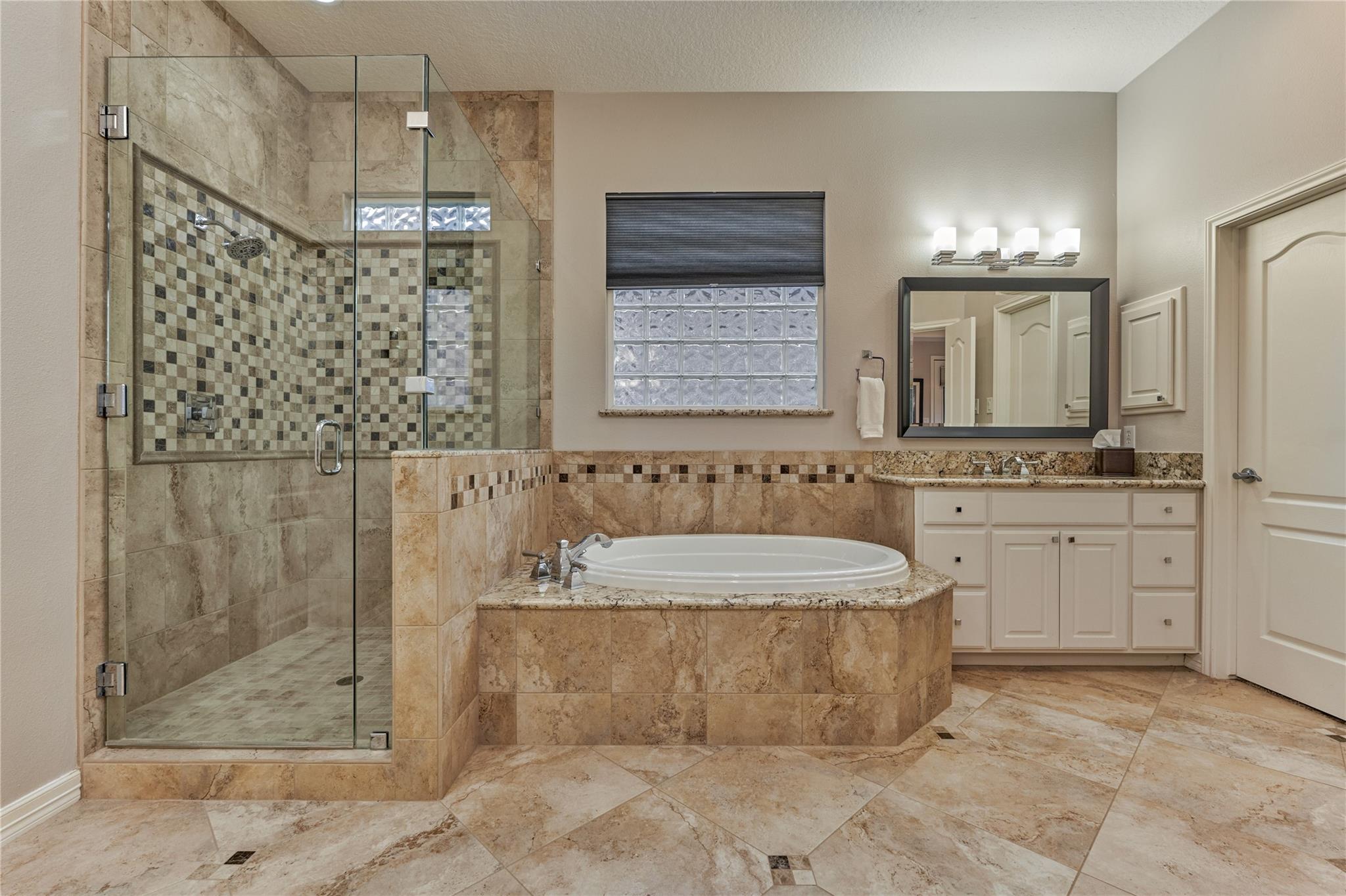 Bathroom with a glass-enclosed shower, tiled soaking tub, and vanity beneath a large mirror.