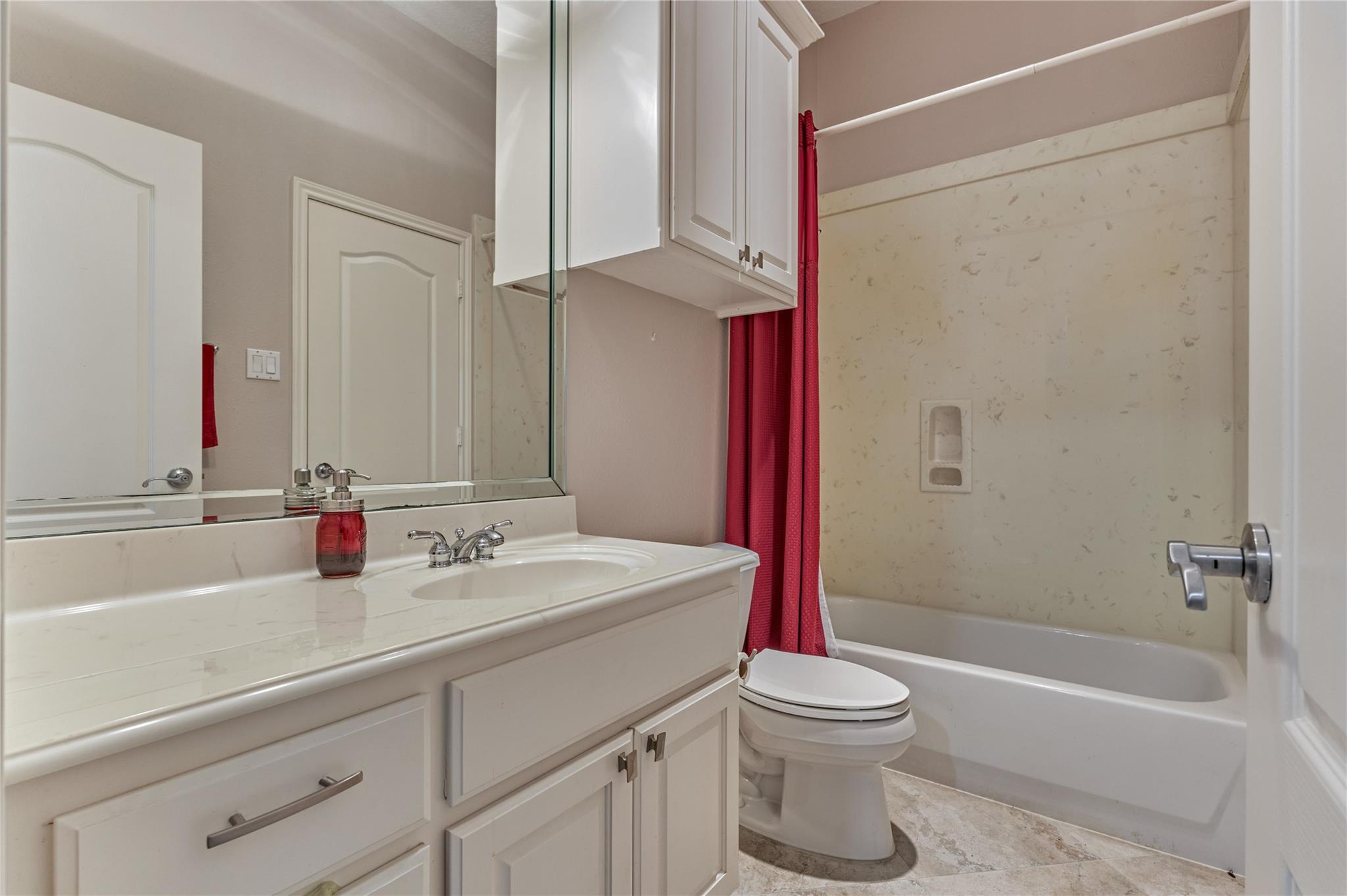 Bathroom with a white vanity, mirrored cabinets, toilet, and bathtub with a red shower curtain.