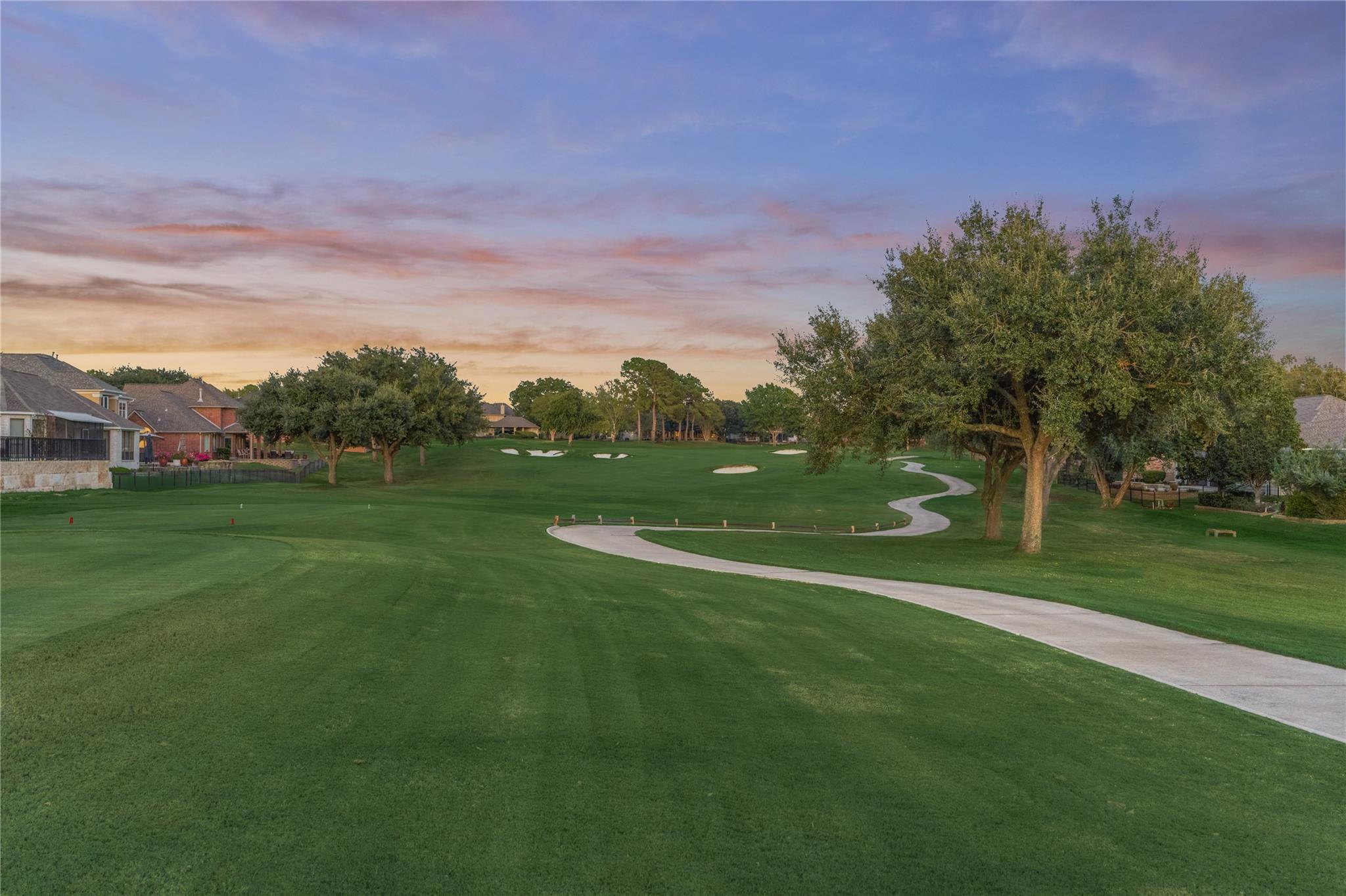 Golf course with a winding cart path, sand bunkers, and mature trees at sunset.