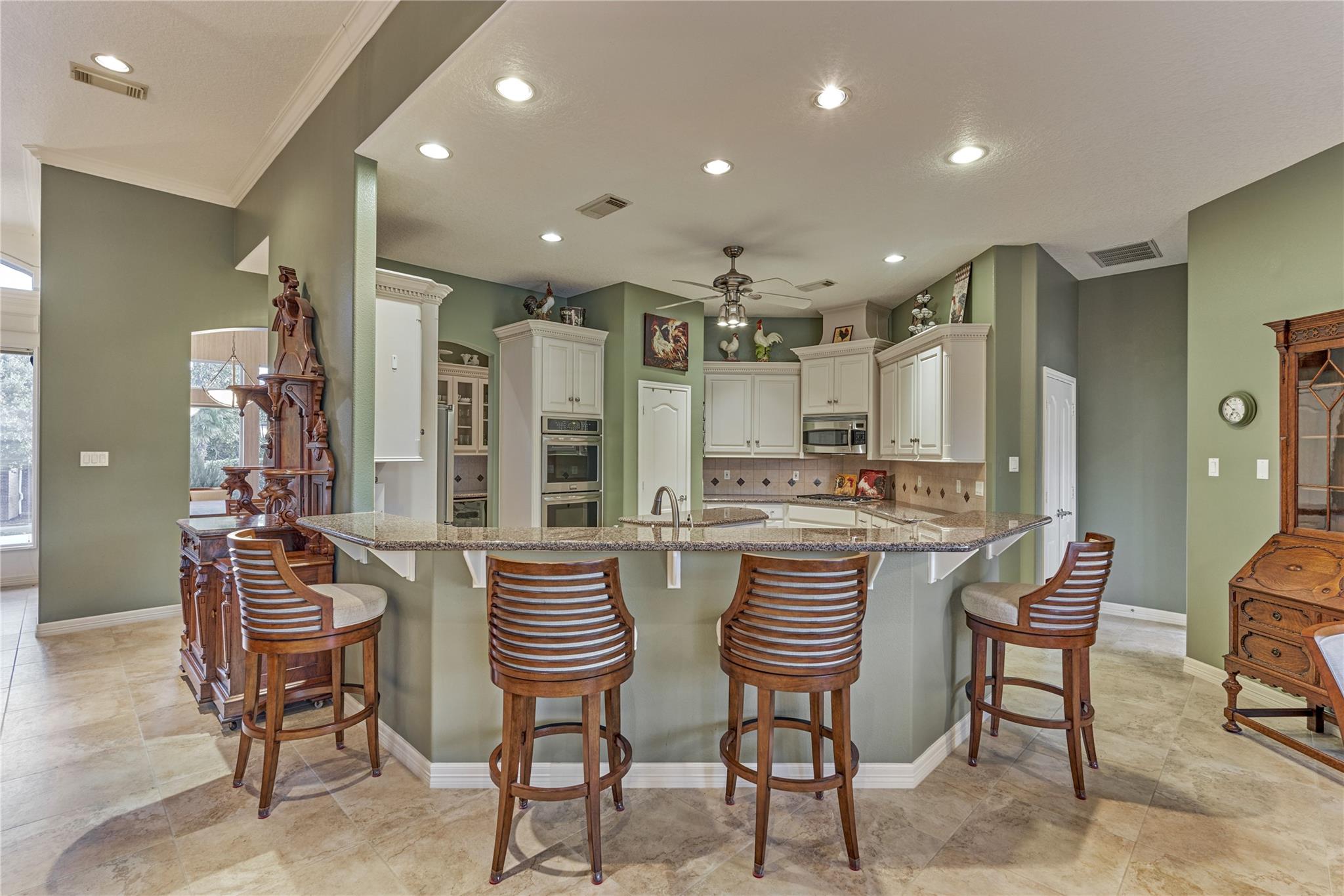Kitchen with a large granite island, four wooden bar stools, sage-green walls and white cabinetry.