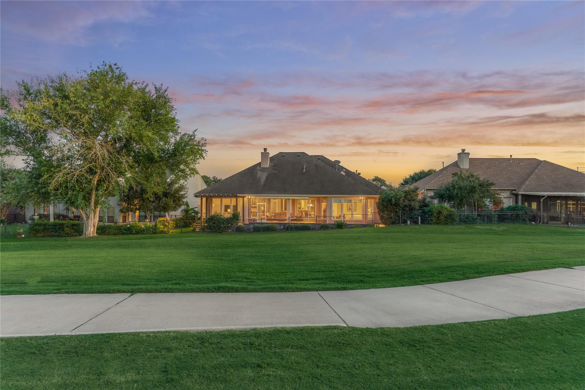 Home’s rear exterior with a covered patio and broad green lawn at sunset.