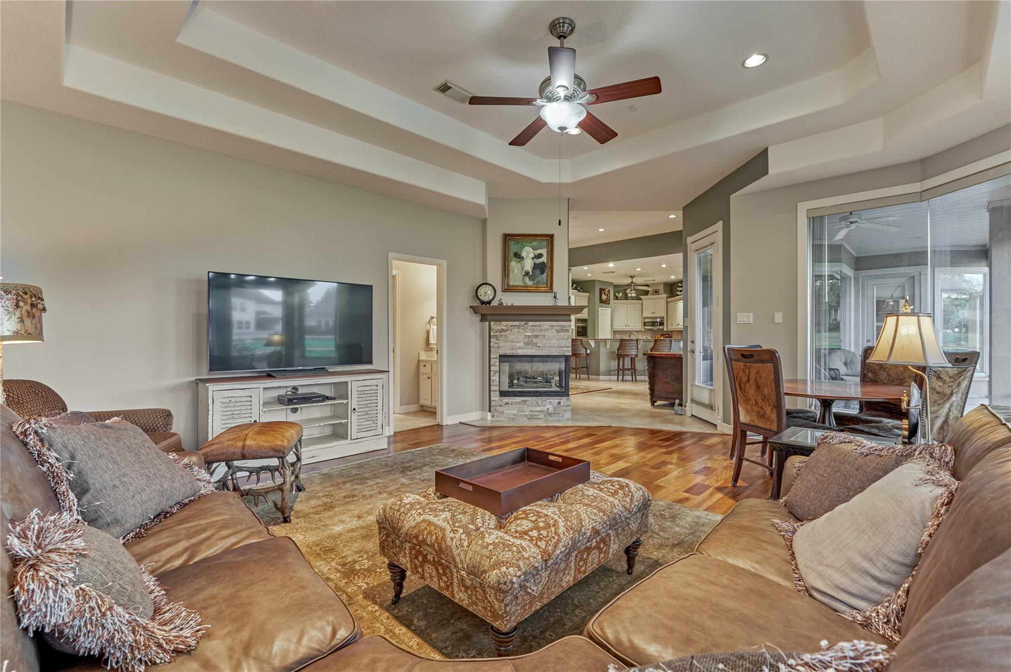 Living room with a stone fireplace, tray ceiling, and open view into the kitchen.