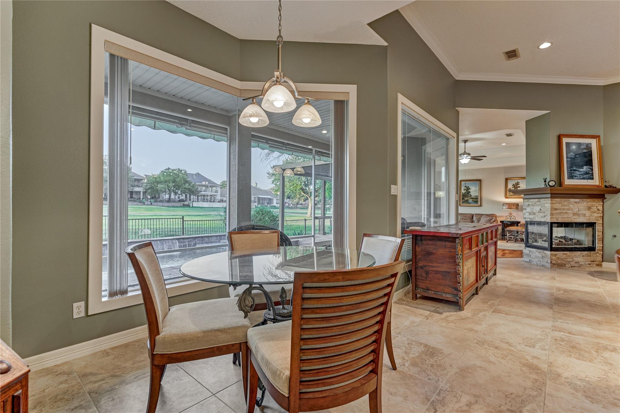 Dining area with a glass-top table beside large windows overlooking a covered patio and lawn.
