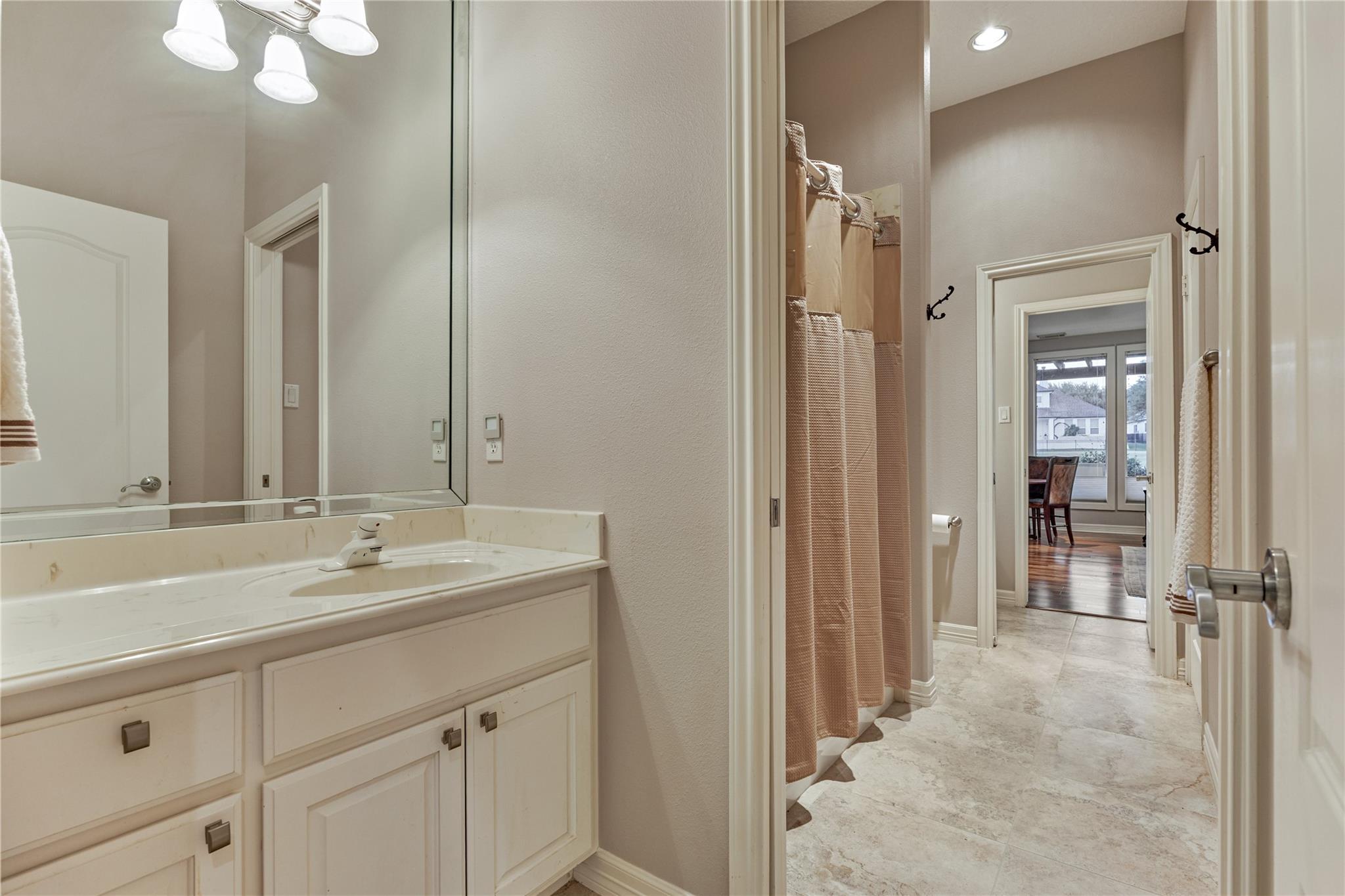 Bathroom with a long white vanity, large mirror, tiled floor, and curtained shower area.