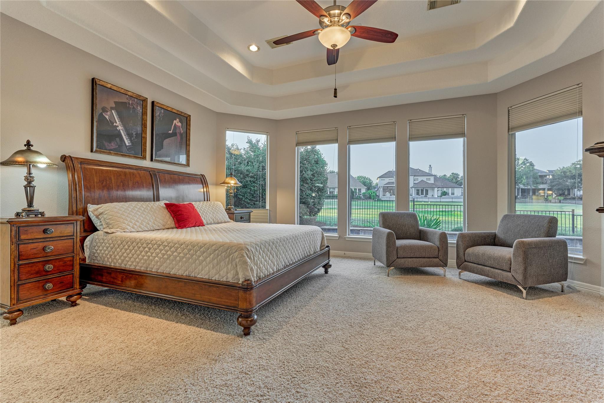Bedroom with a wooden bed and two armchairs beside tall windows overlooking a fenced lawn.