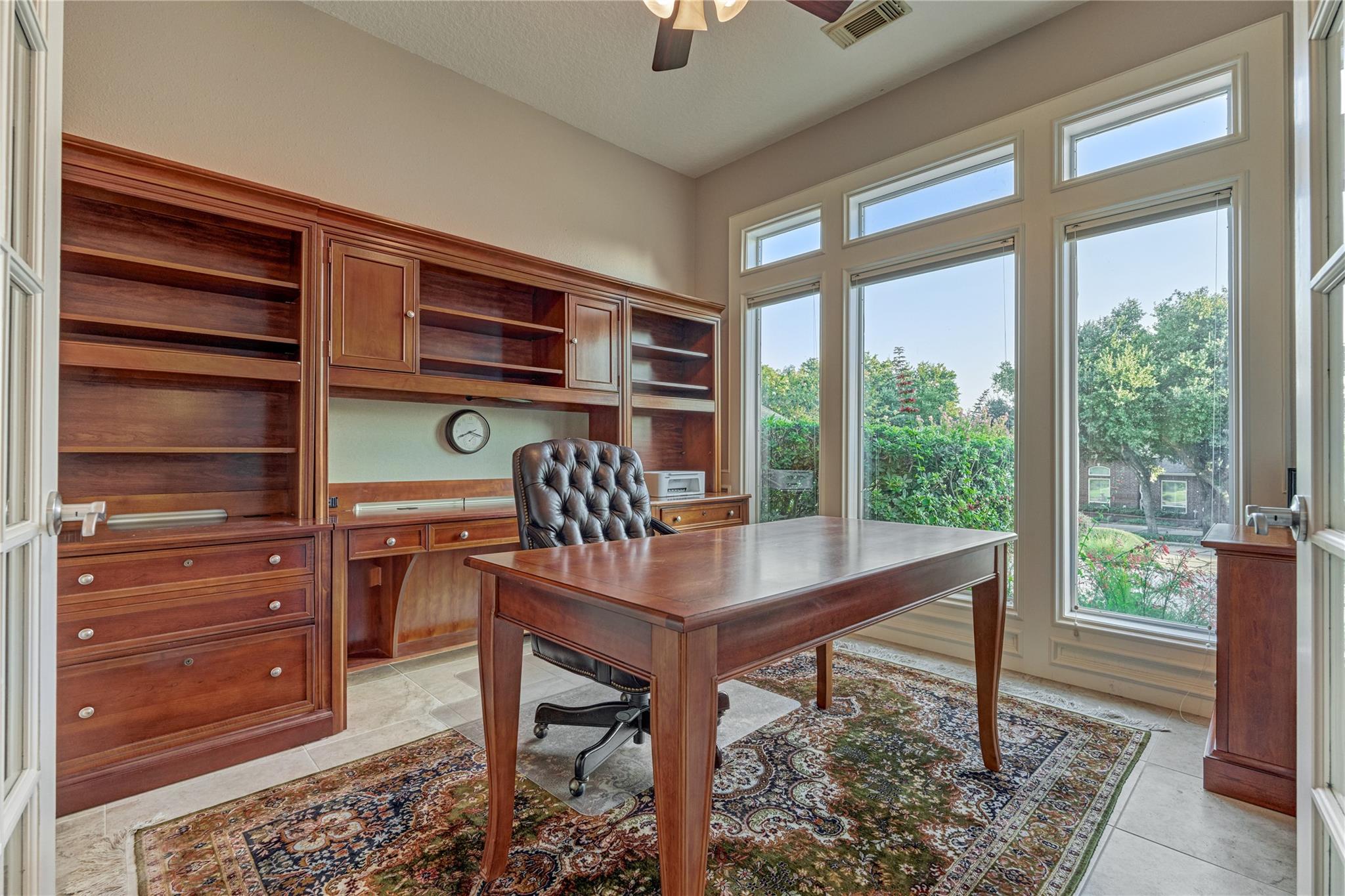 Home office with cherry wood built-ins, a matching desk, and tall windows overlooking greenery.