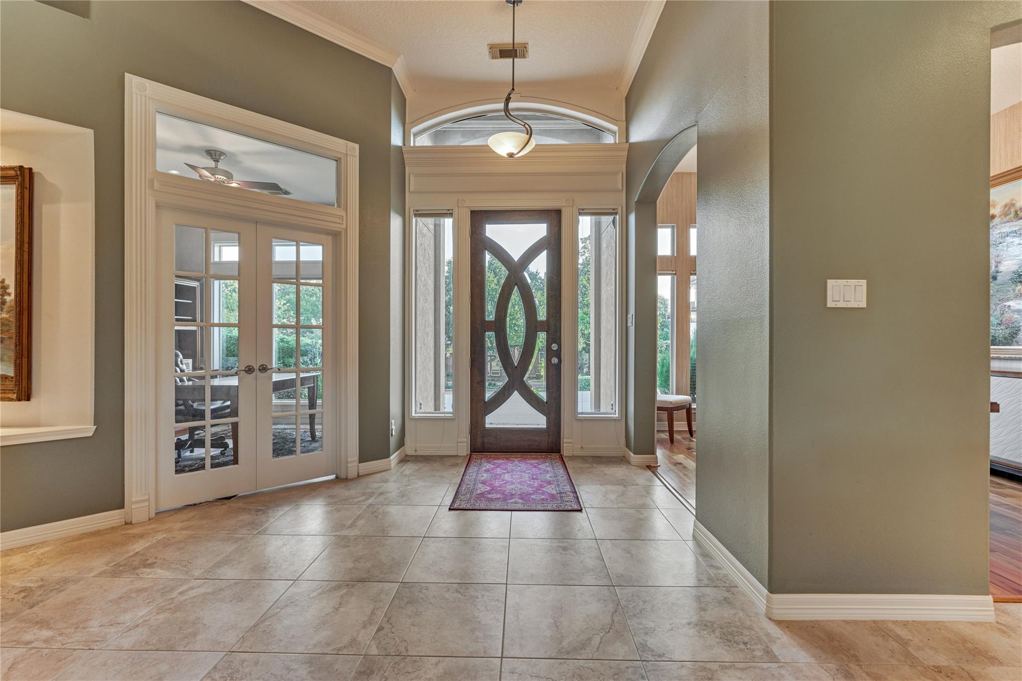 Foyer with a decorative-glass front door, arched transom, French doors, and tiled floor.