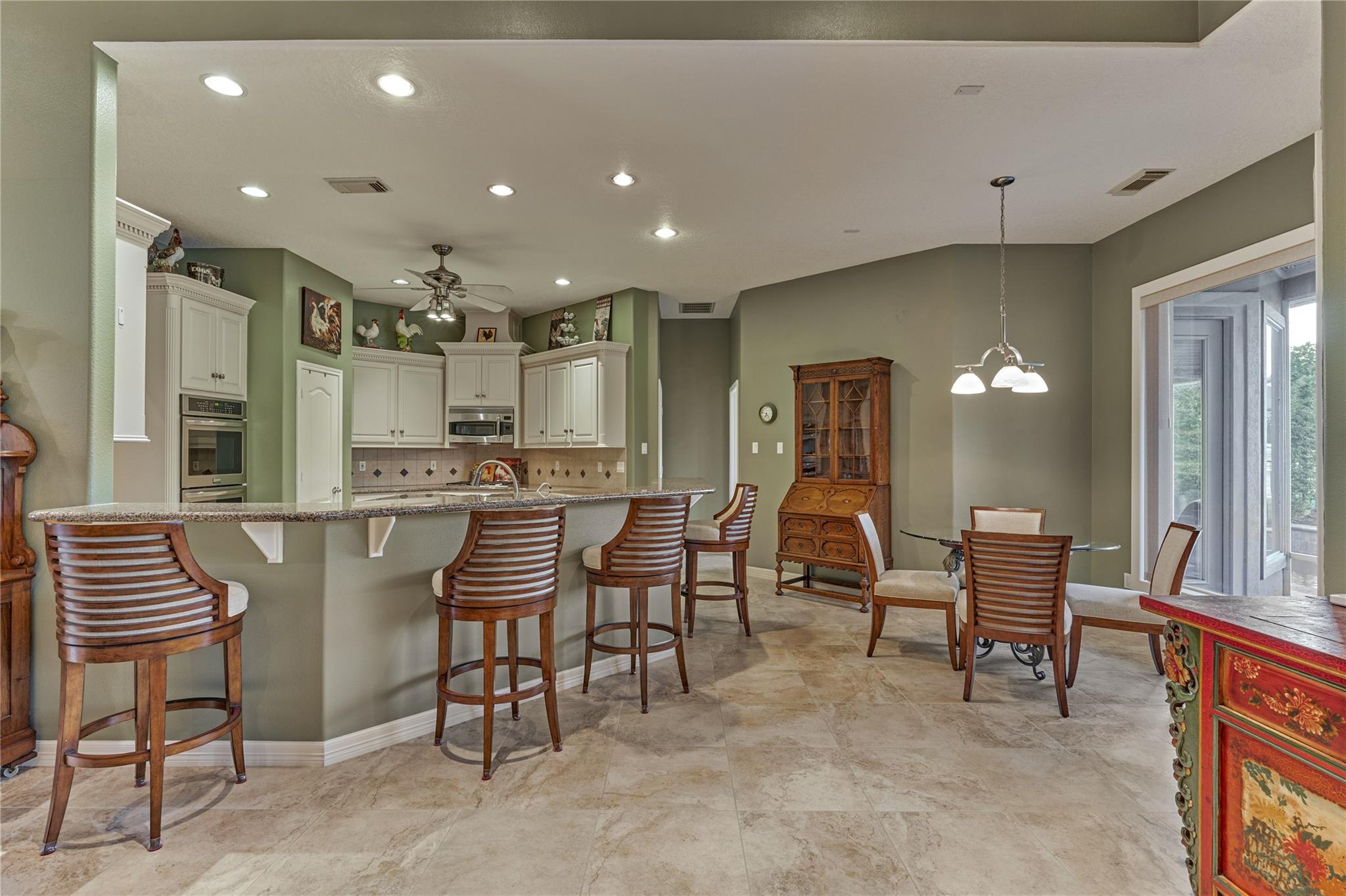 Kitchen and dining area with a granite breakfast bar, white cabinets, wooden stools, and sliding glass doors.
