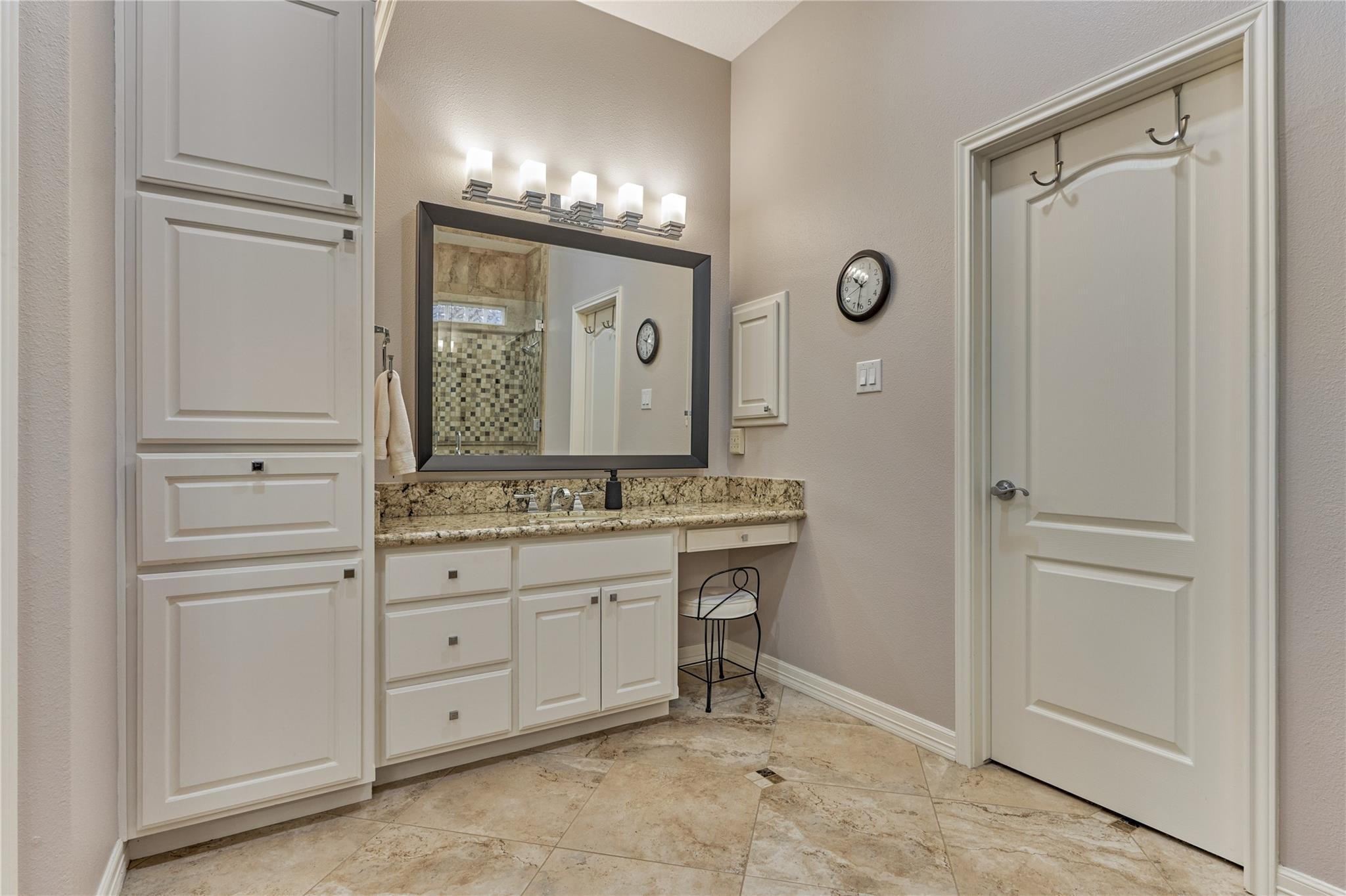 Bathroom vanity with white cabinetry, granite countertop, large mirror, and stone tile floor.