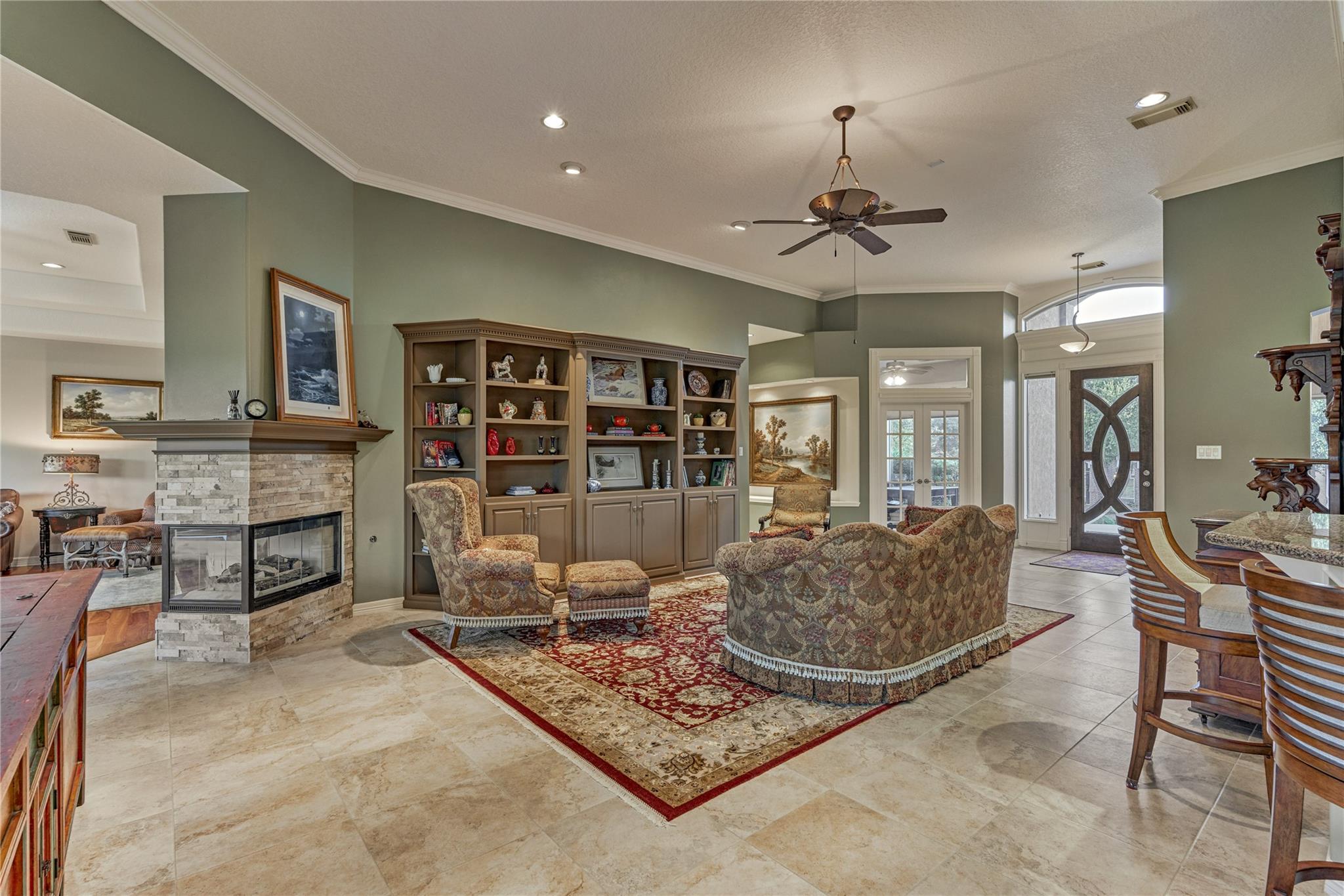 Furnished living room with a stone fireplace, built-in shelves, and patterned seating around a large rug.