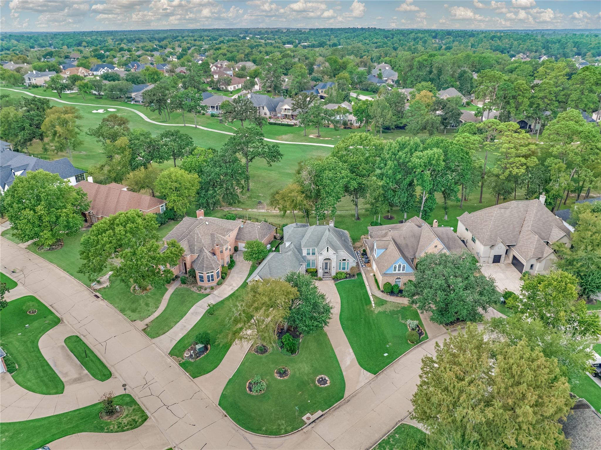 Aerial view of a home beside a golf course, surrounded by tree-lined streets and landscaped lawns.