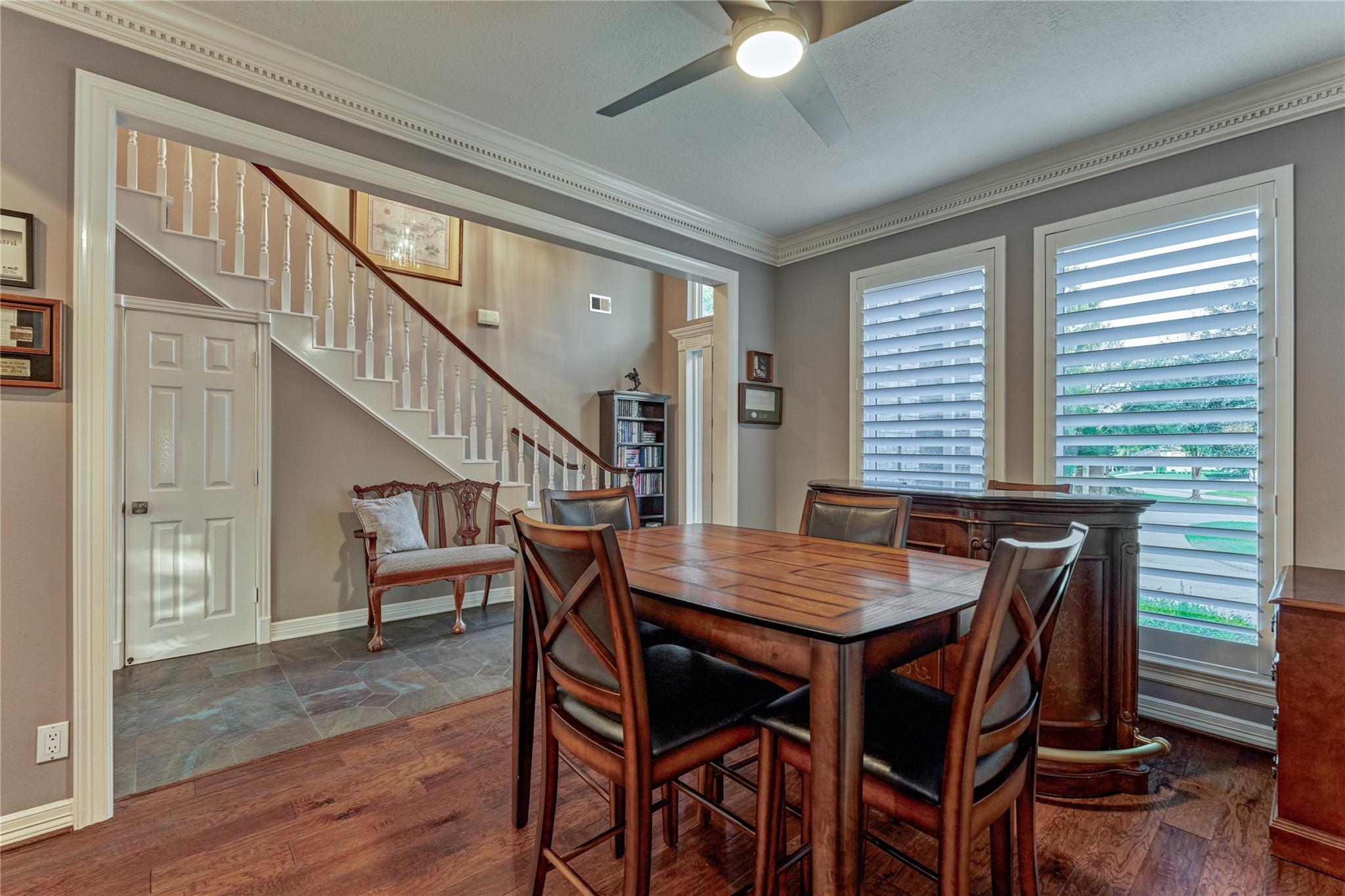 Dining room with a dark wood table beside shuttered windows and a staircase.