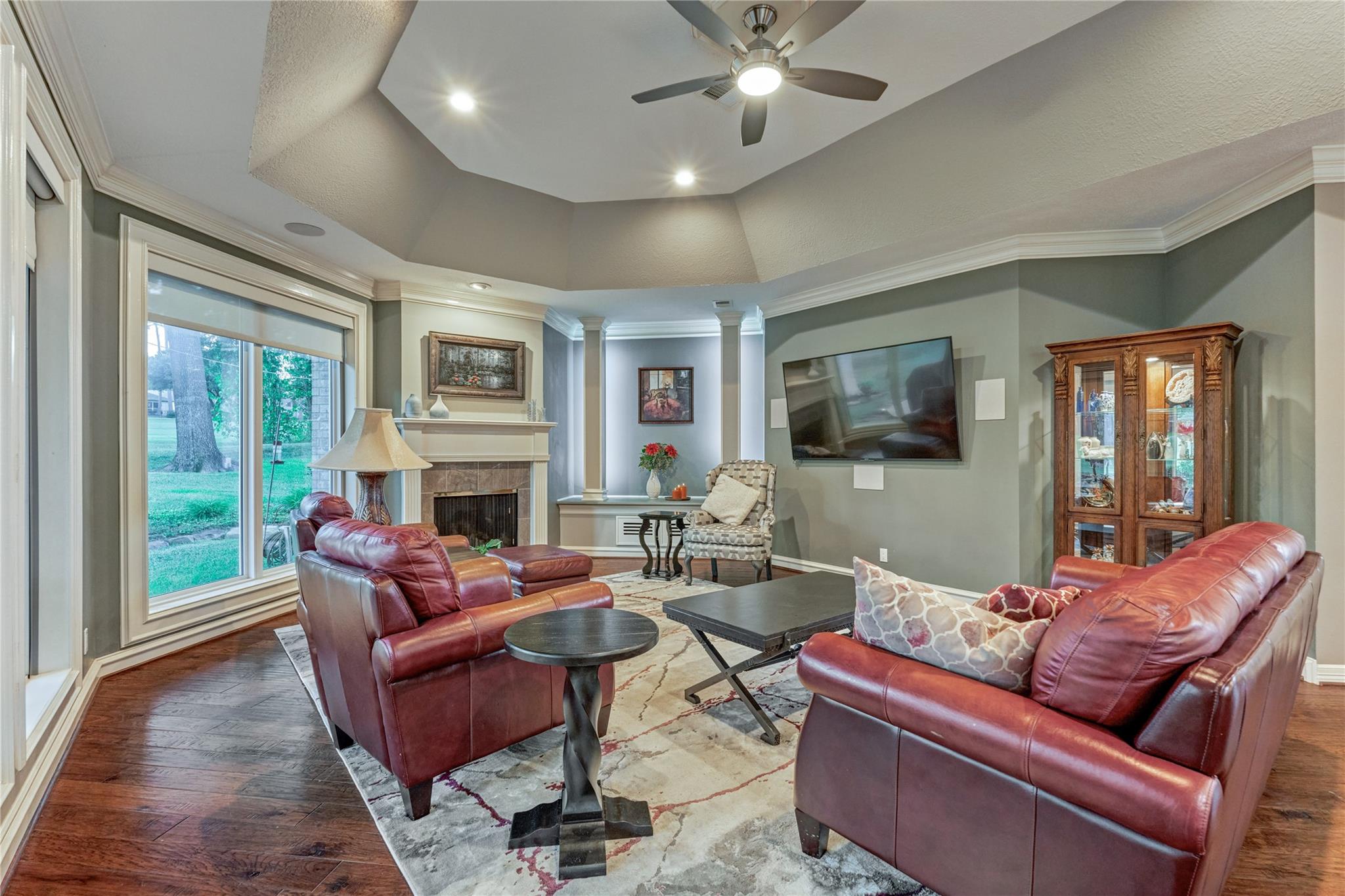 Living room with burgundy leather sofas, a fireplace, and large windows overlooking the lawn.