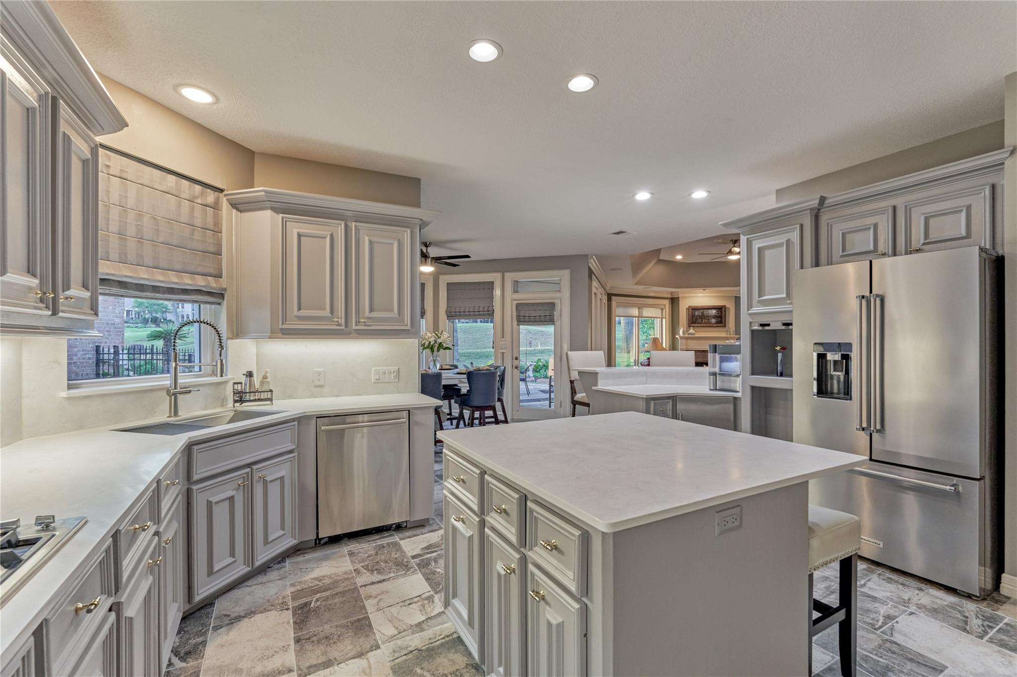 Kitchen with gray paneled cabinets, a large white island, and stainless steel appliances.