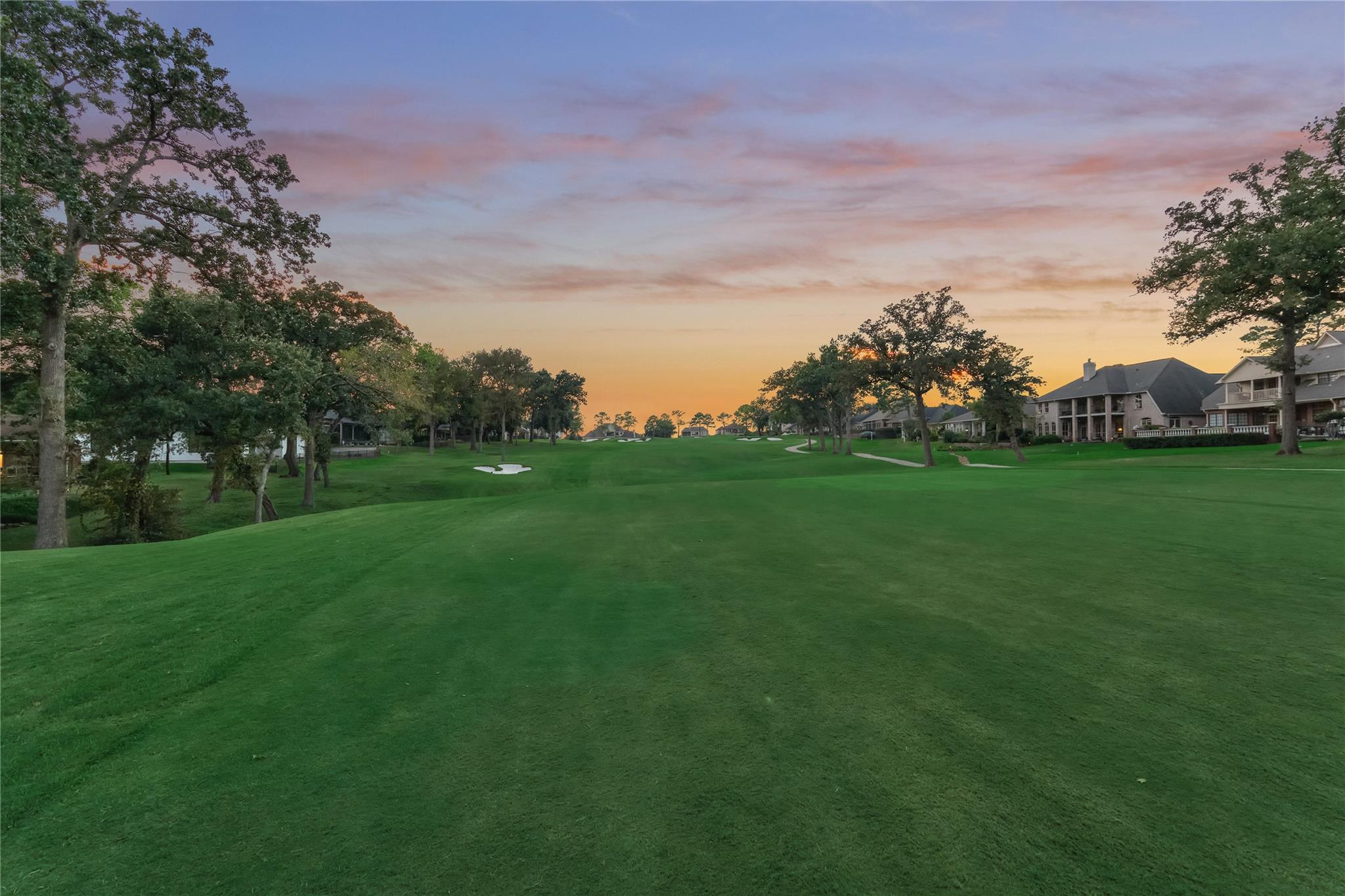 Golf course fairway at dusk, with a sand bunker and homes along the right side.