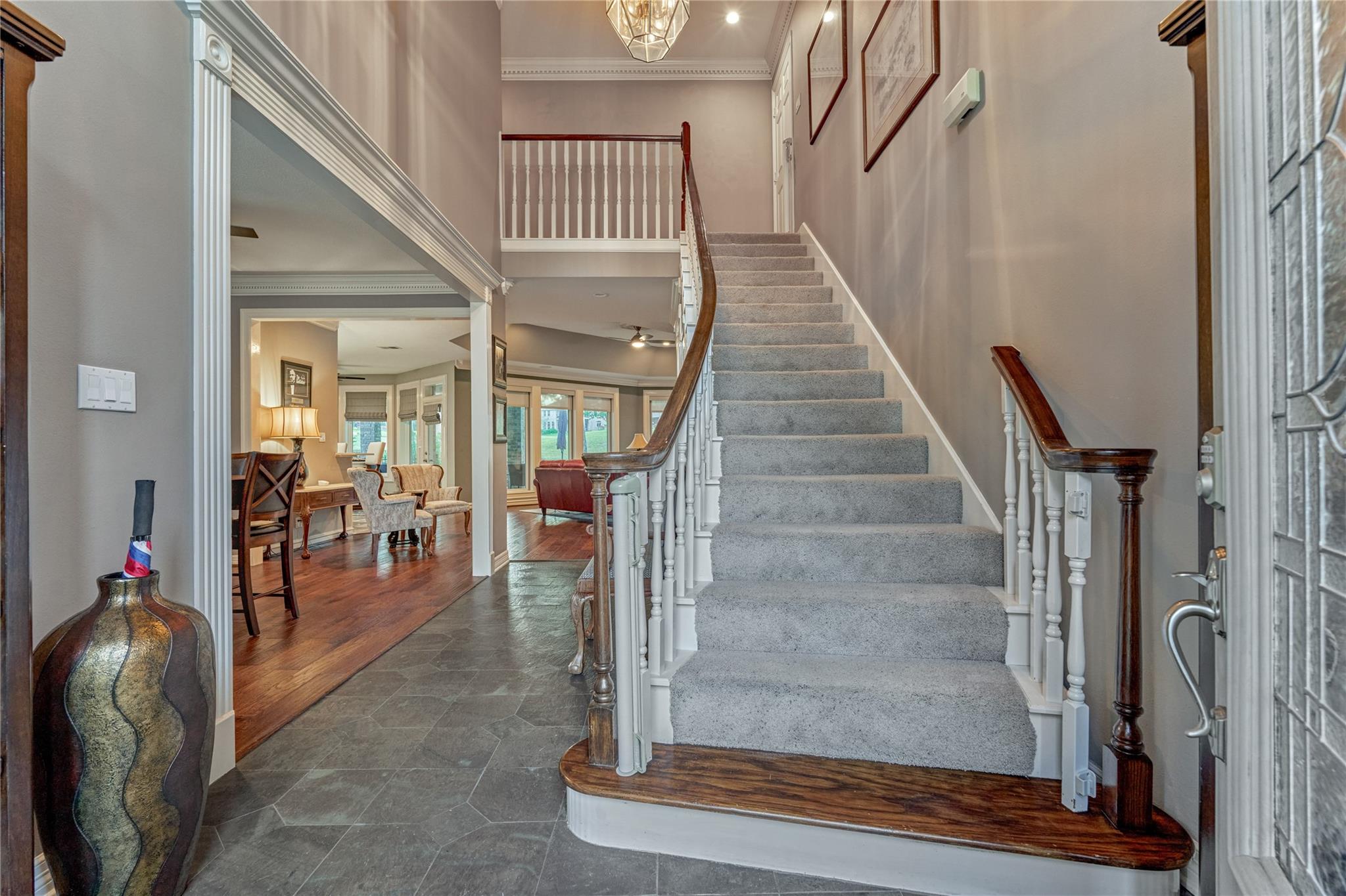Entry foyer with a carpeted staircase, dark wood rails, and open views into furnished living and dining areas.