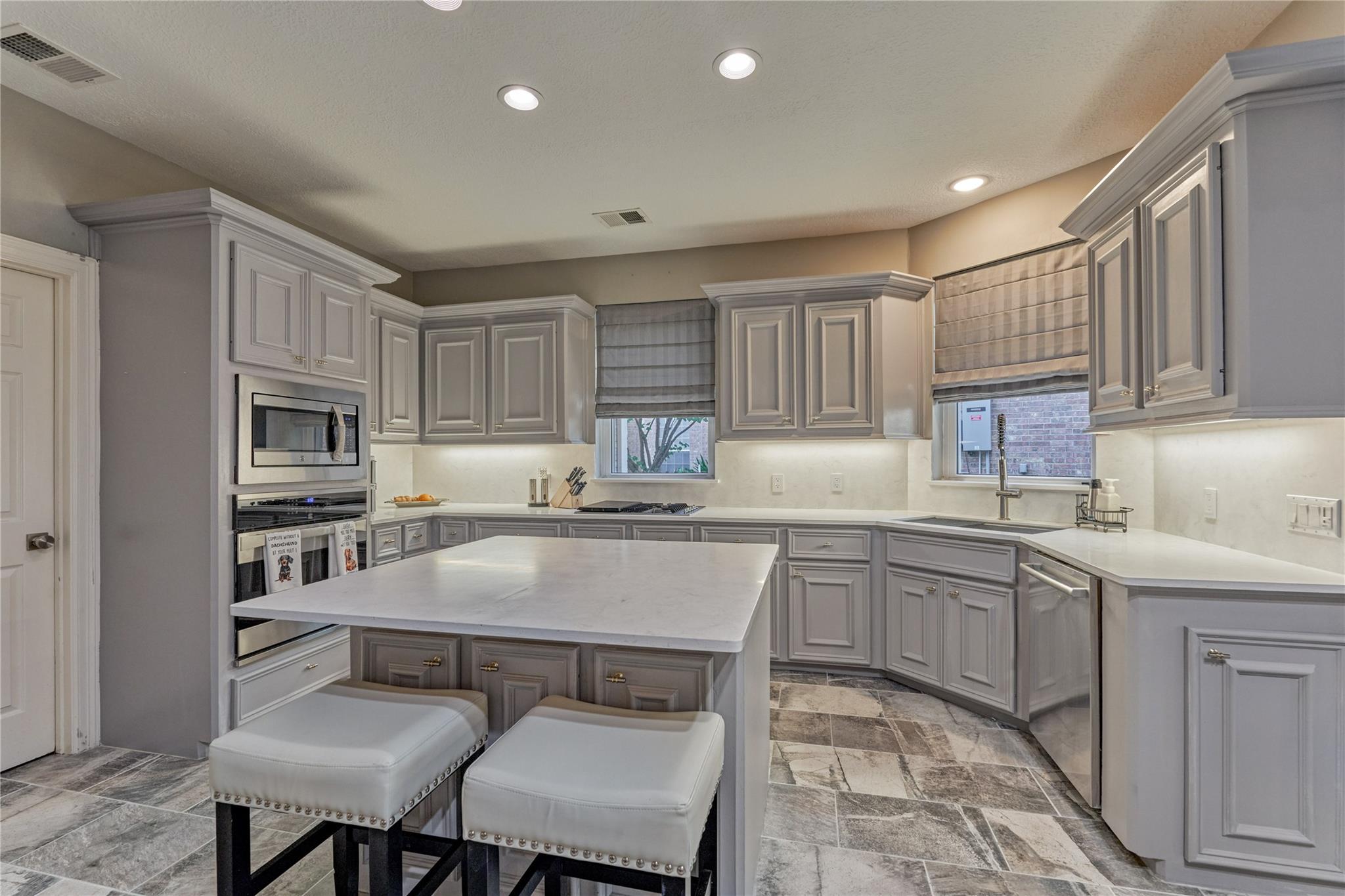Kitchen with gray cabinetry, a large island, built-in ovens, and stone-patterned tile flooring.