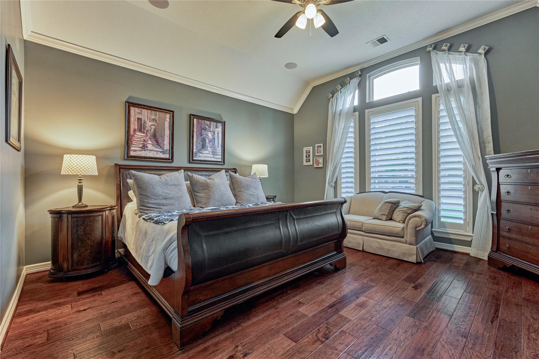 Bedroom with a dark wood sleigh bed, hardwood floors, and tall shuttered windows beside a loveseat.