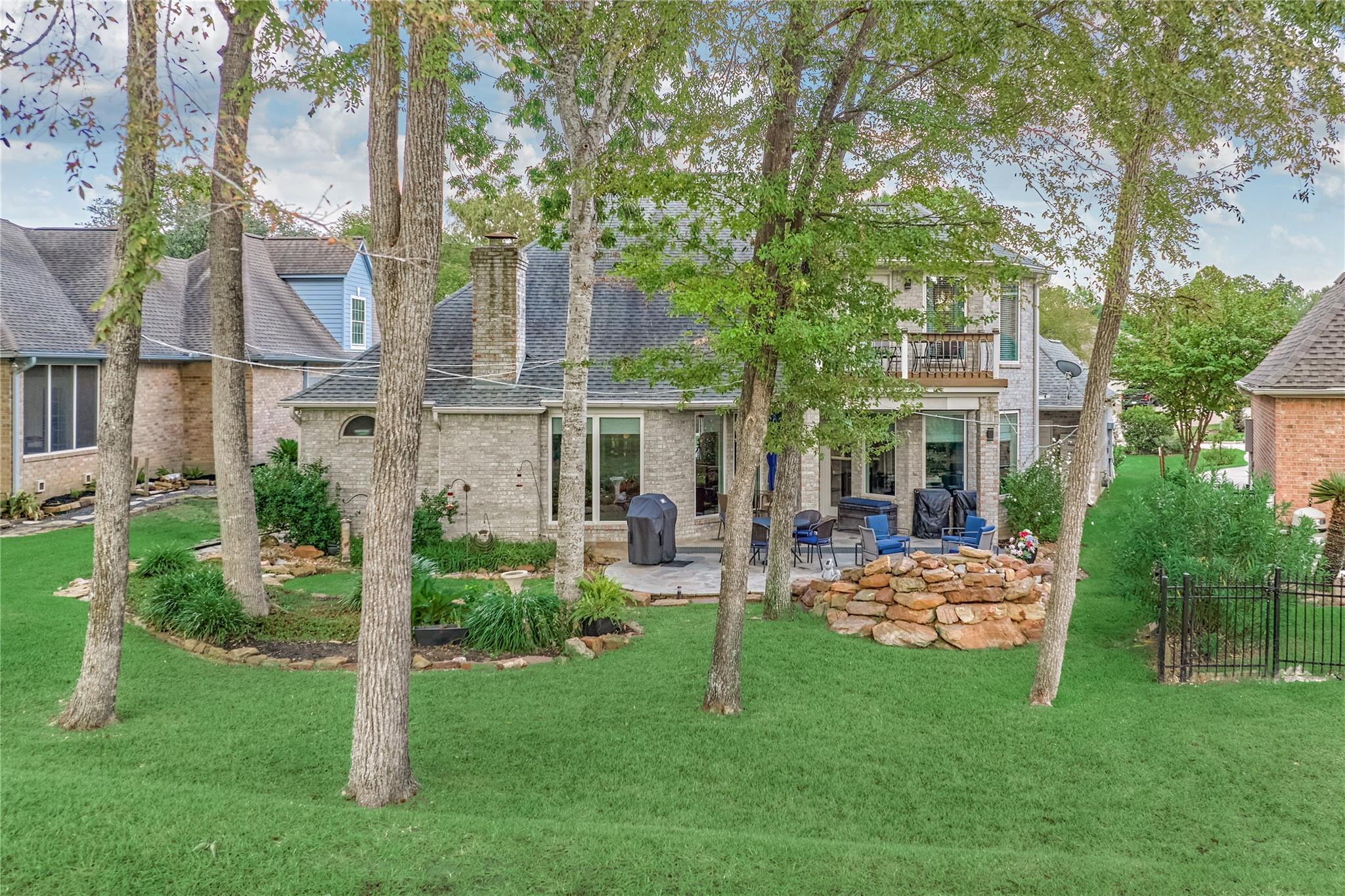 Brick house rear patio with outdoor seating, mature trees, and a broad green lawn.