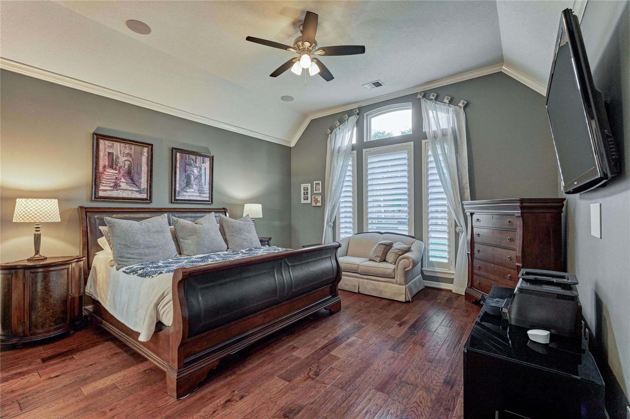 Furnished bedroom with a dark wood bed, hardwood floors, and tall shuttered windows.