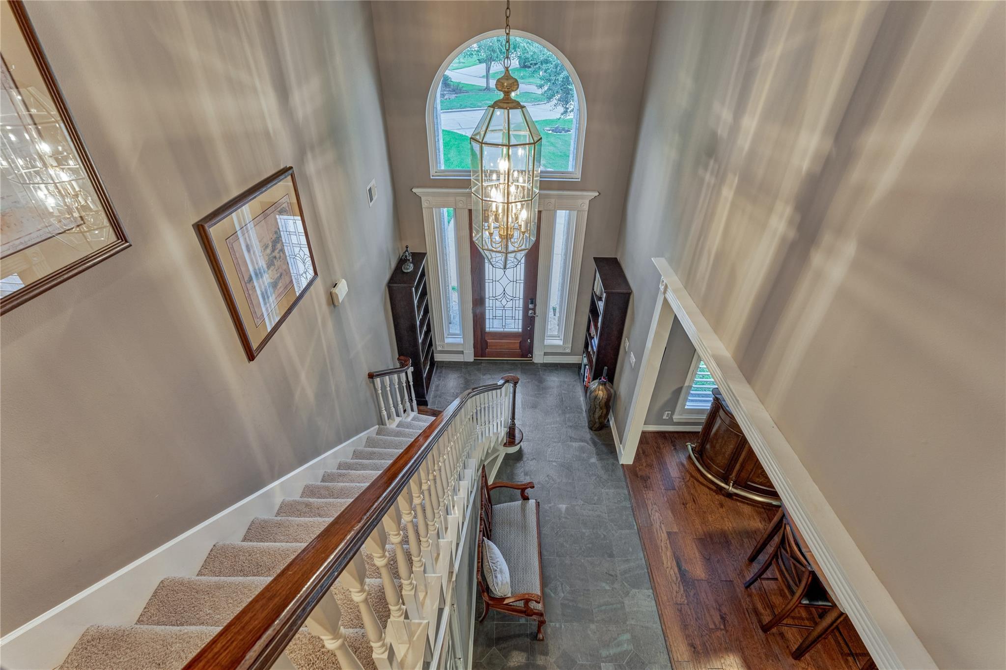Two-story foyer with a curved staircase, large chandelier, and arched window above the entry door.