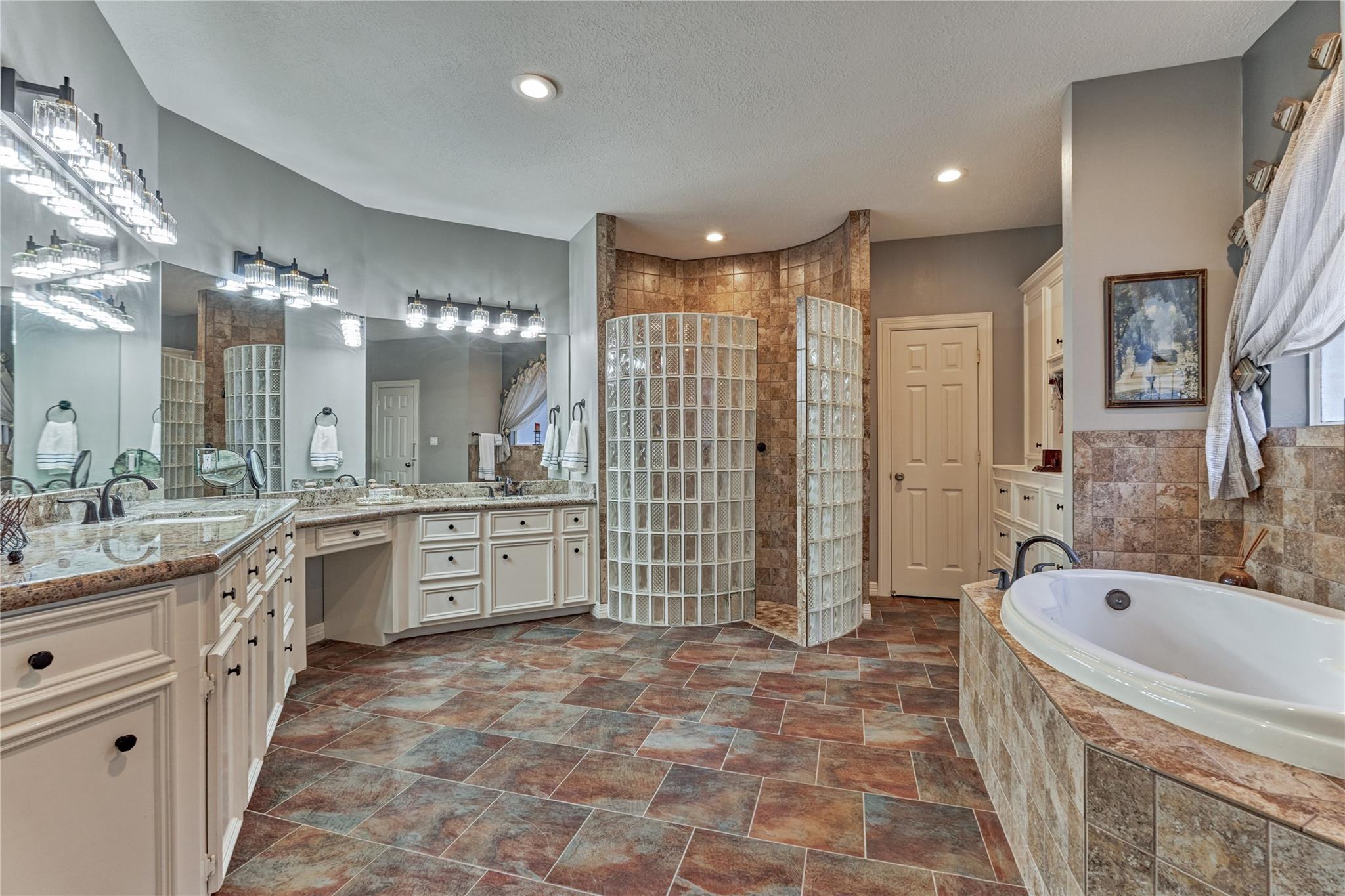 Spacious bathroom with a glass-block shower, double vanity, and large tiled soaking tub.